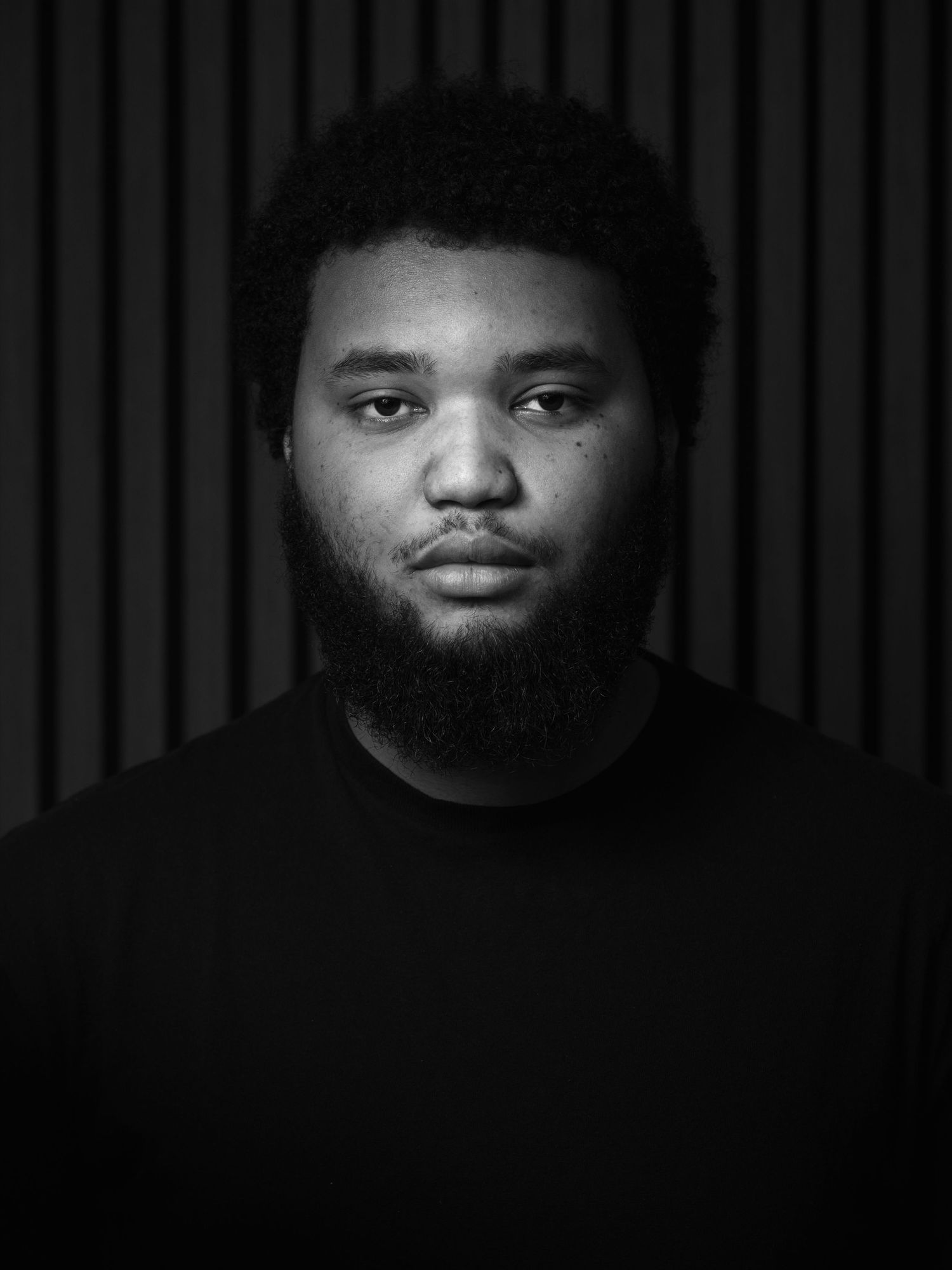 Black and white portrait with dramatic lighting against striped background.