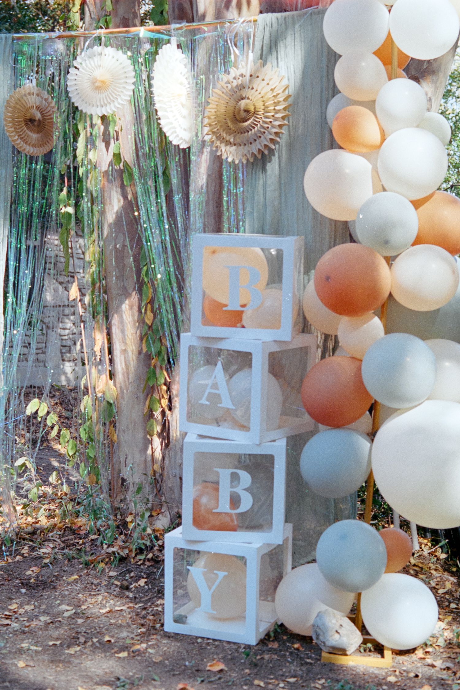 Baby shower decorations featuring white stacked alphabet blocks, balloon garlands in peach and white, and greenery accents.