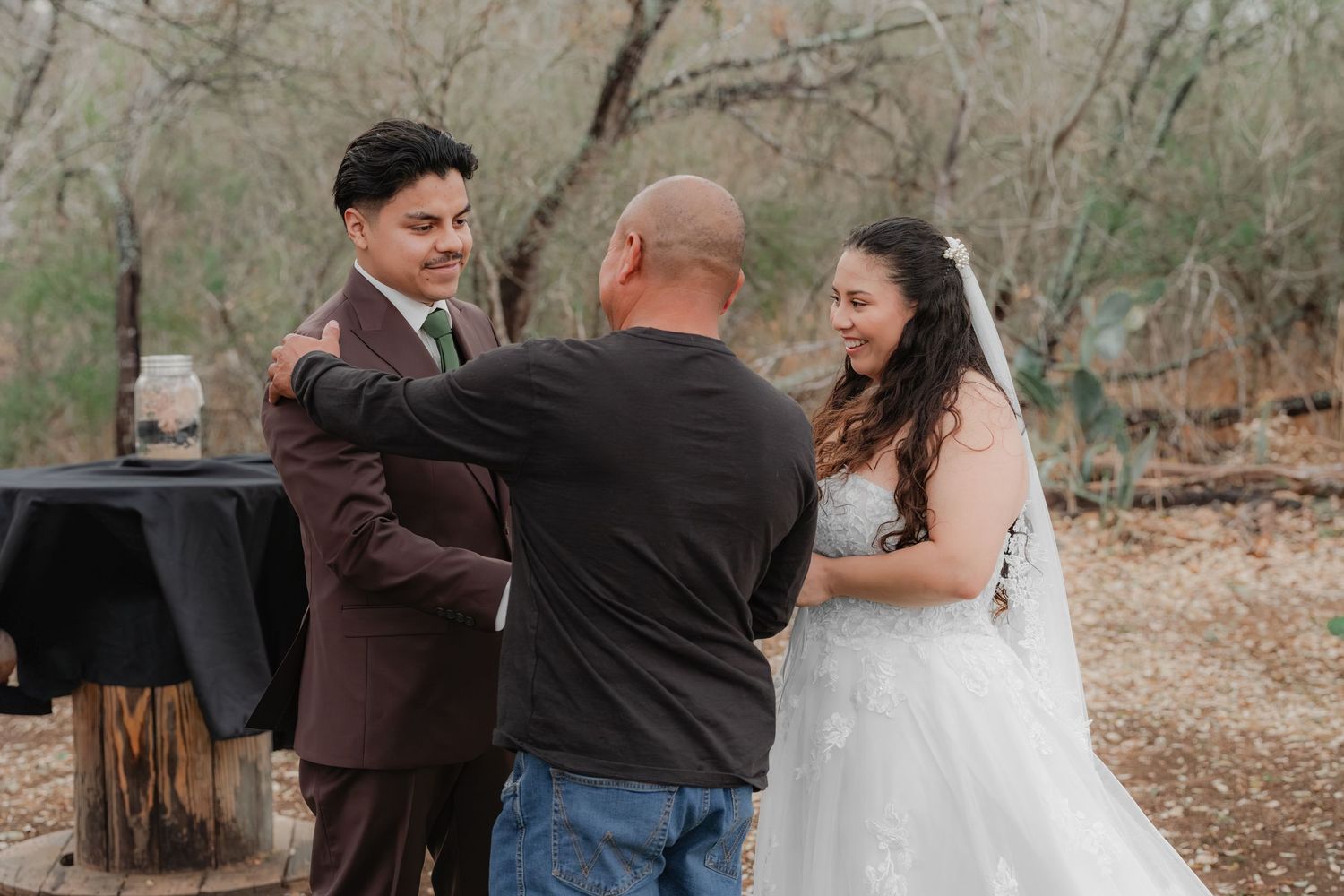 Outdoor wedding celebration with father handing off bride—smiling bride and groom in formal attire, candid moment