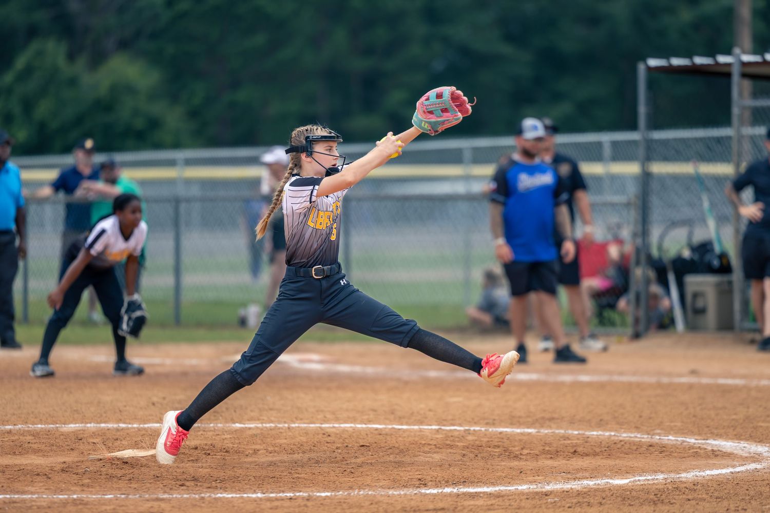 Action shot of a youth softball pitcher mid-throw on the mound during a daylight game