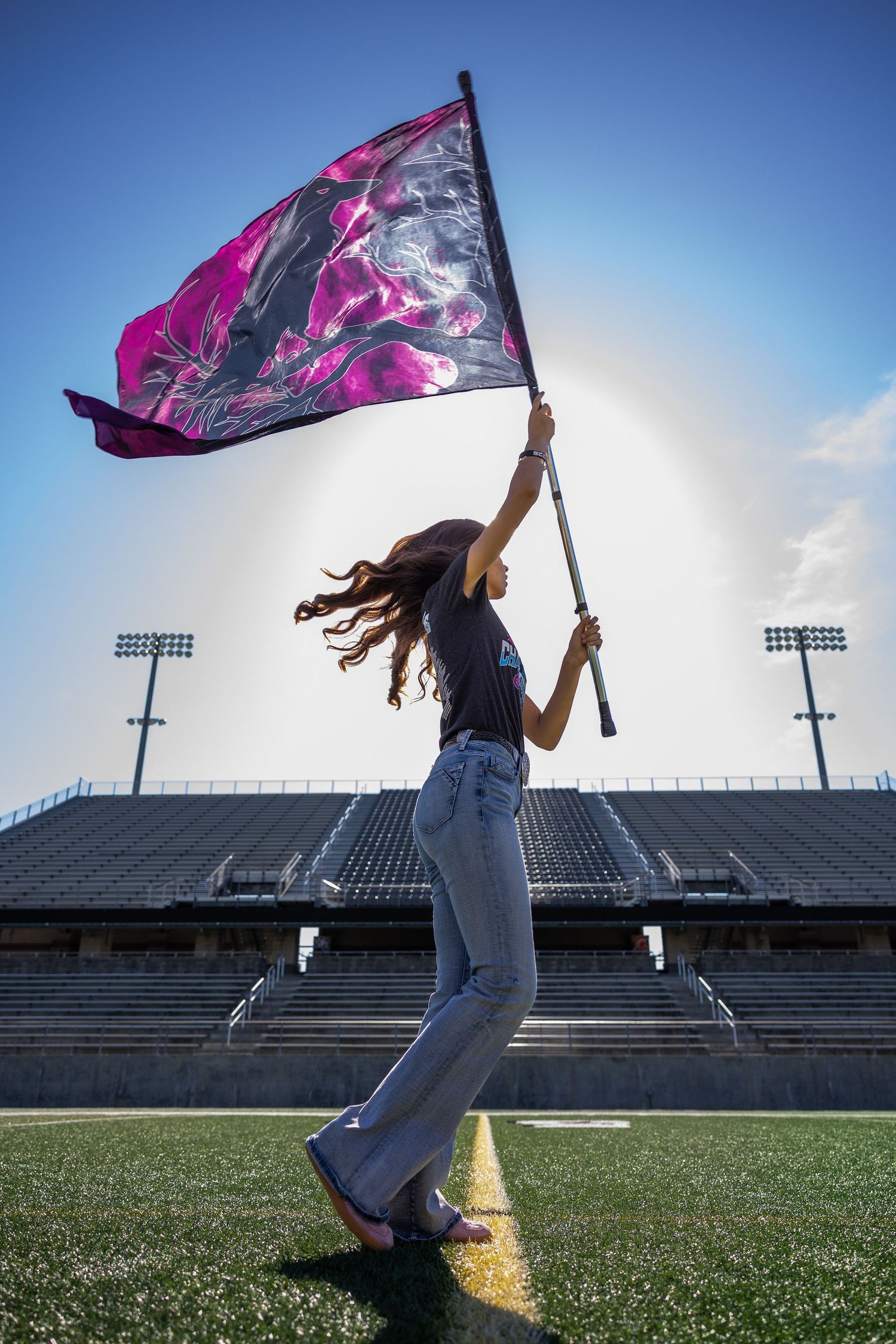 A person holding up a large purple and black flag on an athletic field under a blue sky