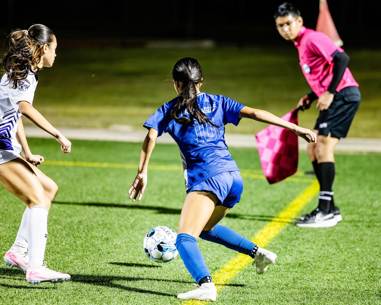 Two youth girl soccer players competing for the ball during an evening game under stadium lights