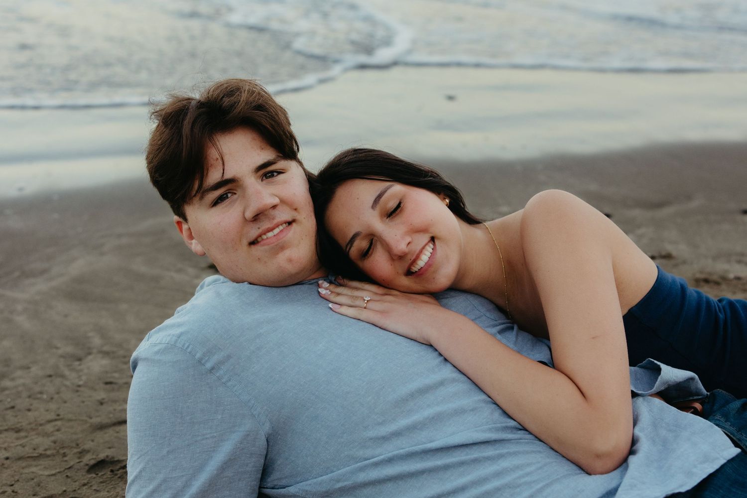 Happy couple relaxing on the beach, woman resting her head on mans shoulder while smiling warmly.