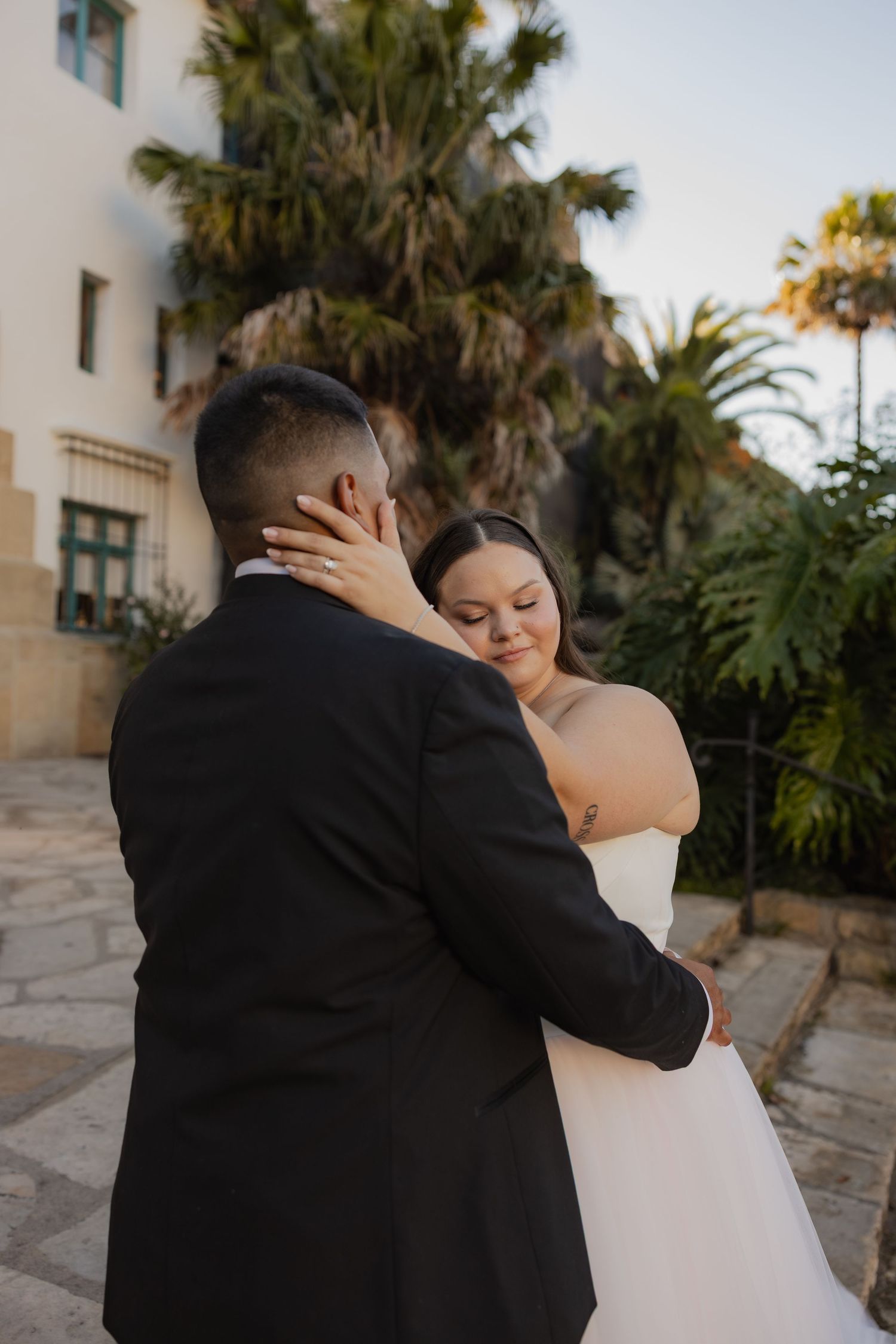 Bride embracing groom near a palm tree at golden hour during outdoor wedding portraits.