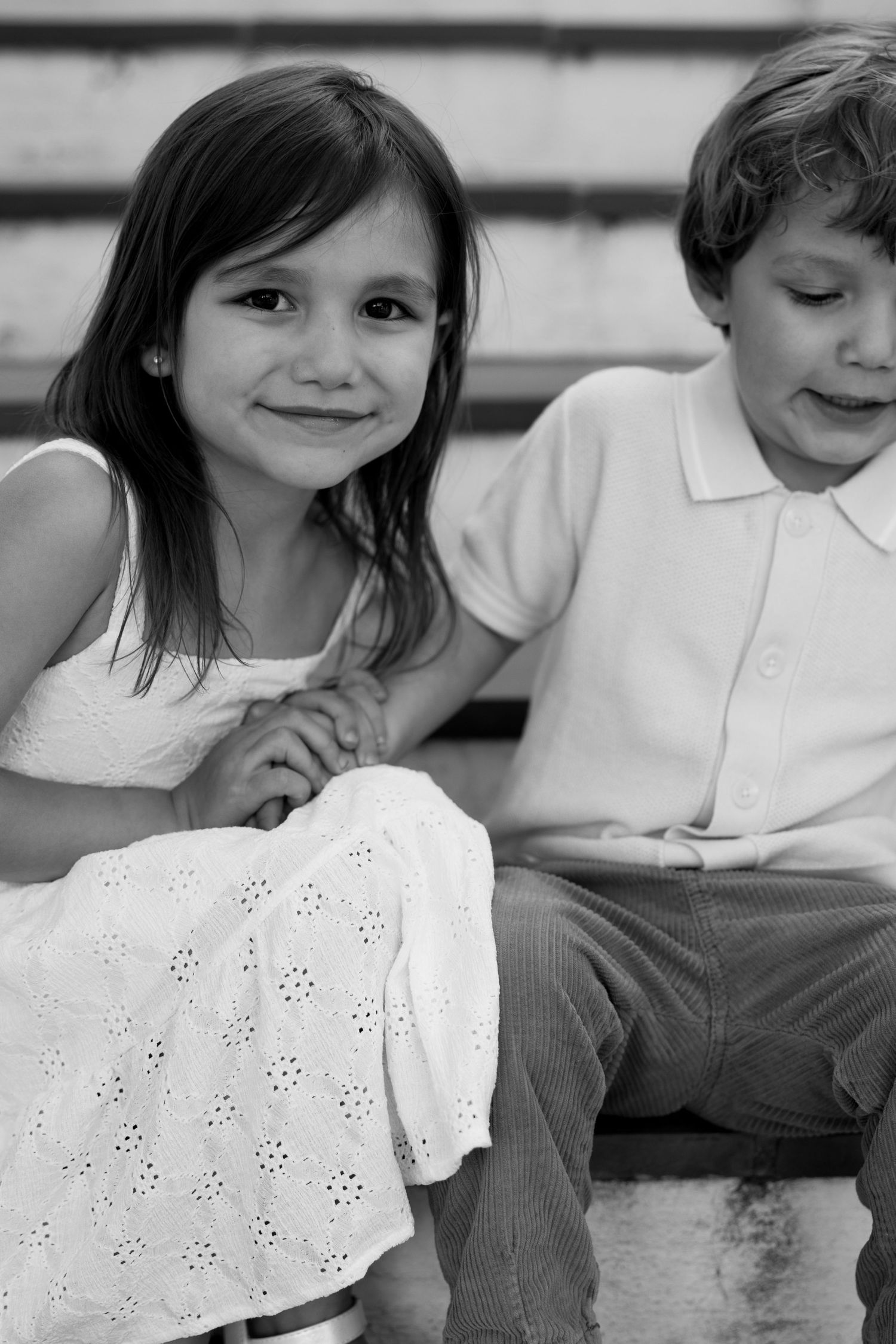 Black and white portrait of a smiling girl in white dress sitting beside a young boy.