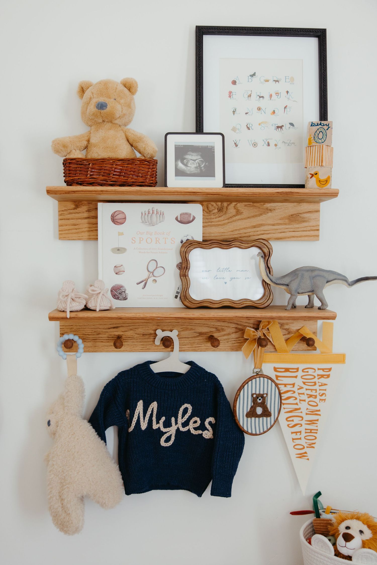 Wooden nursery shelves decorated with teddy bear, ultrasound photo, and a navy Myles sweater.