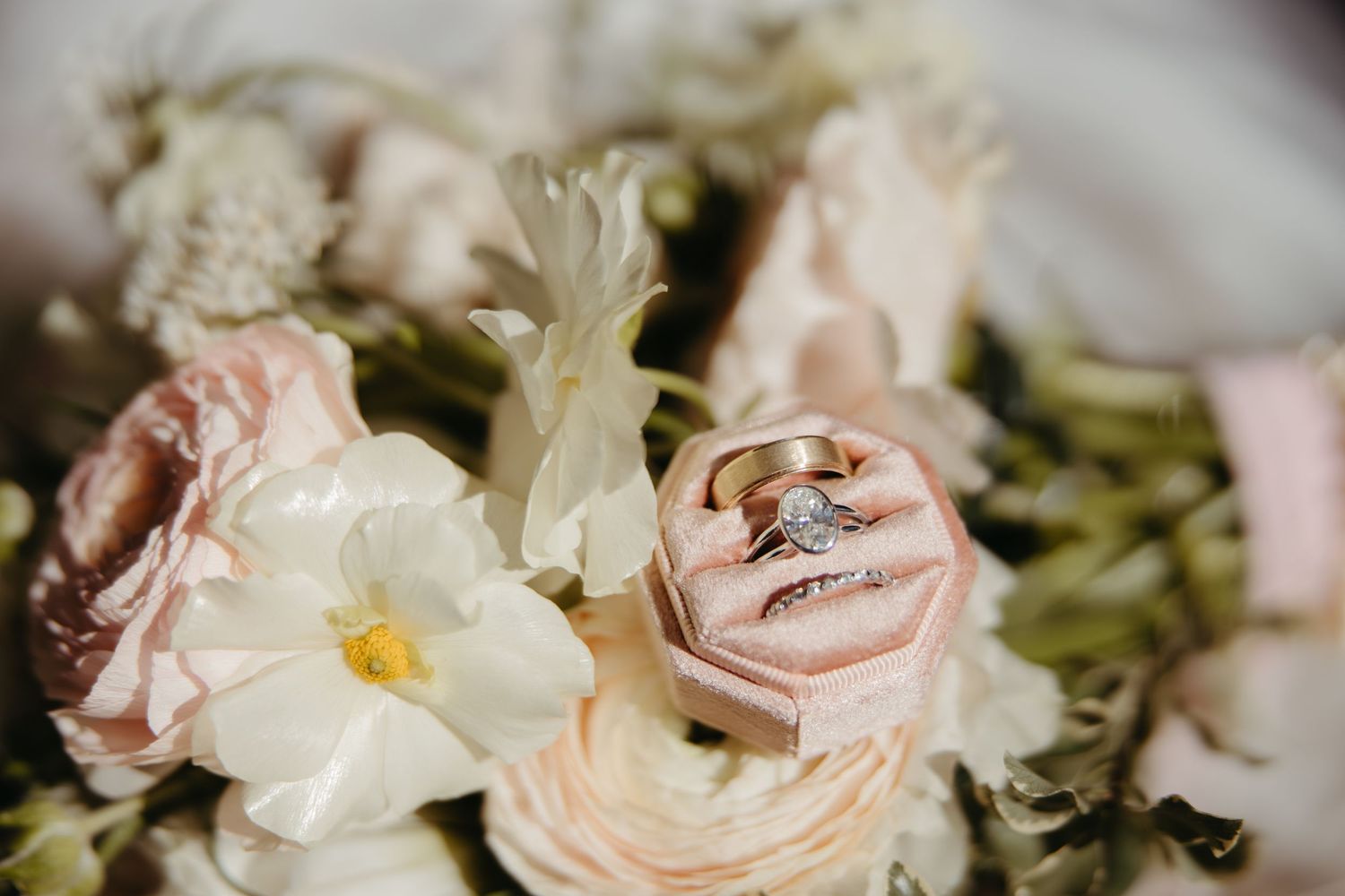 Wedding rings in a pink velvet box nestled among blush and white flowers.