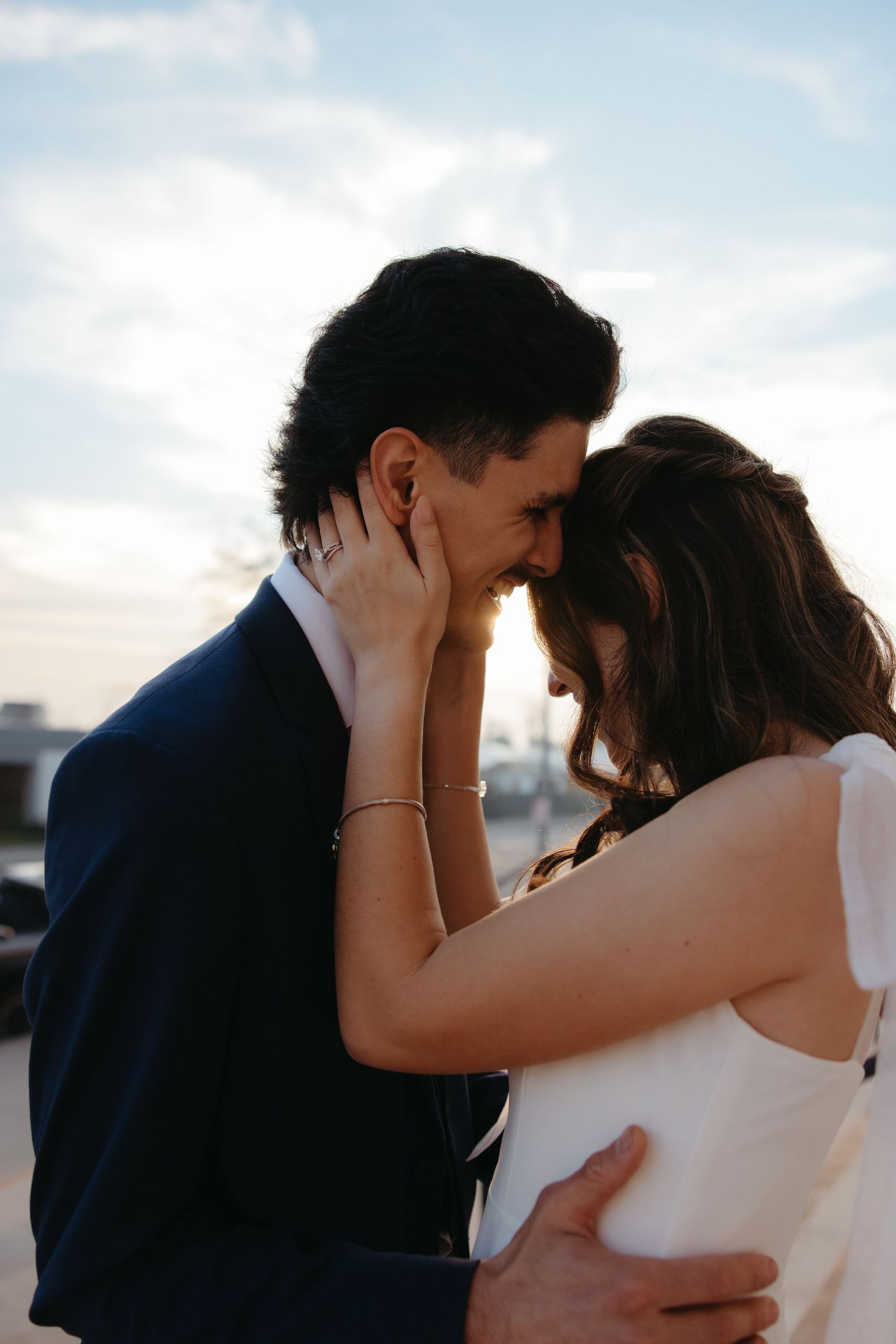 Bride and groom leaning in for a kiss silhouetted against blue sky during golden hour wedding portraits.