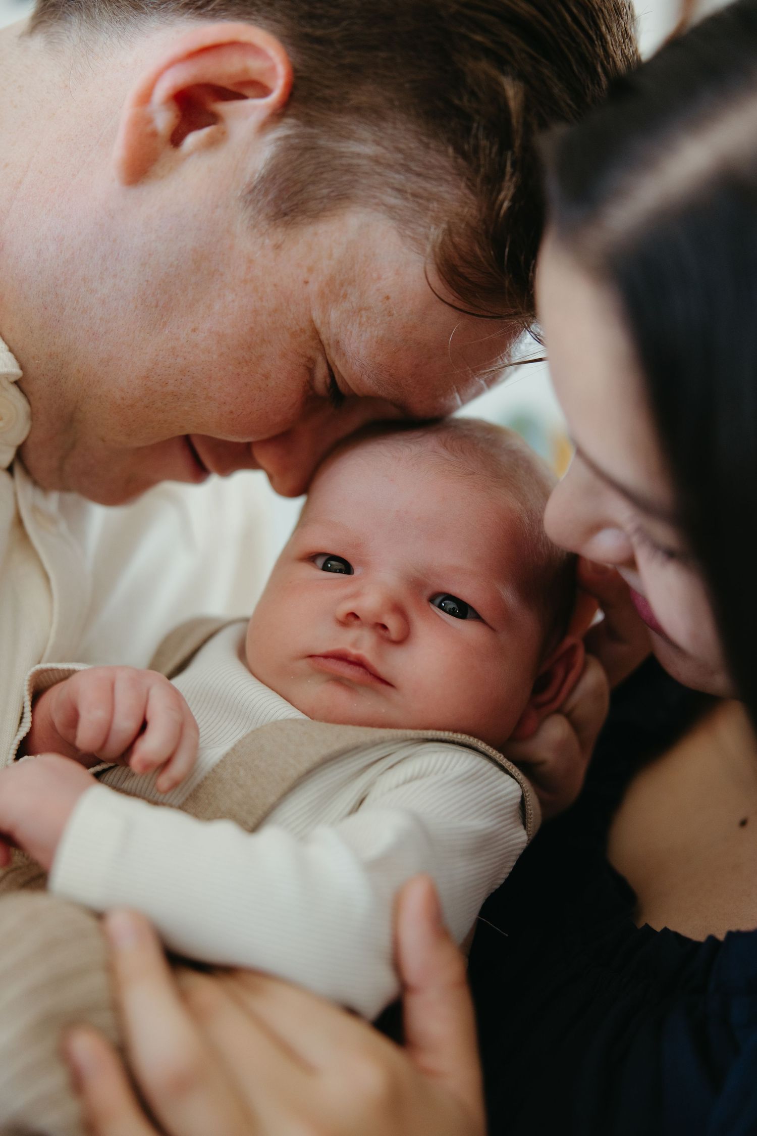 Loving parents tenderly touch foreheads with their alert newborn baby in a close portrait.