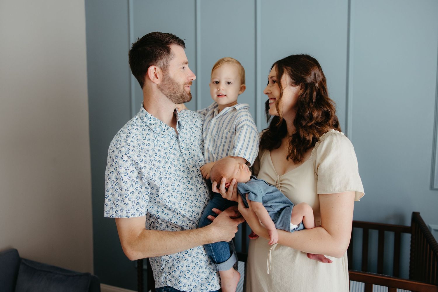 Young family with baby smiling together in a softly lit nursery room.