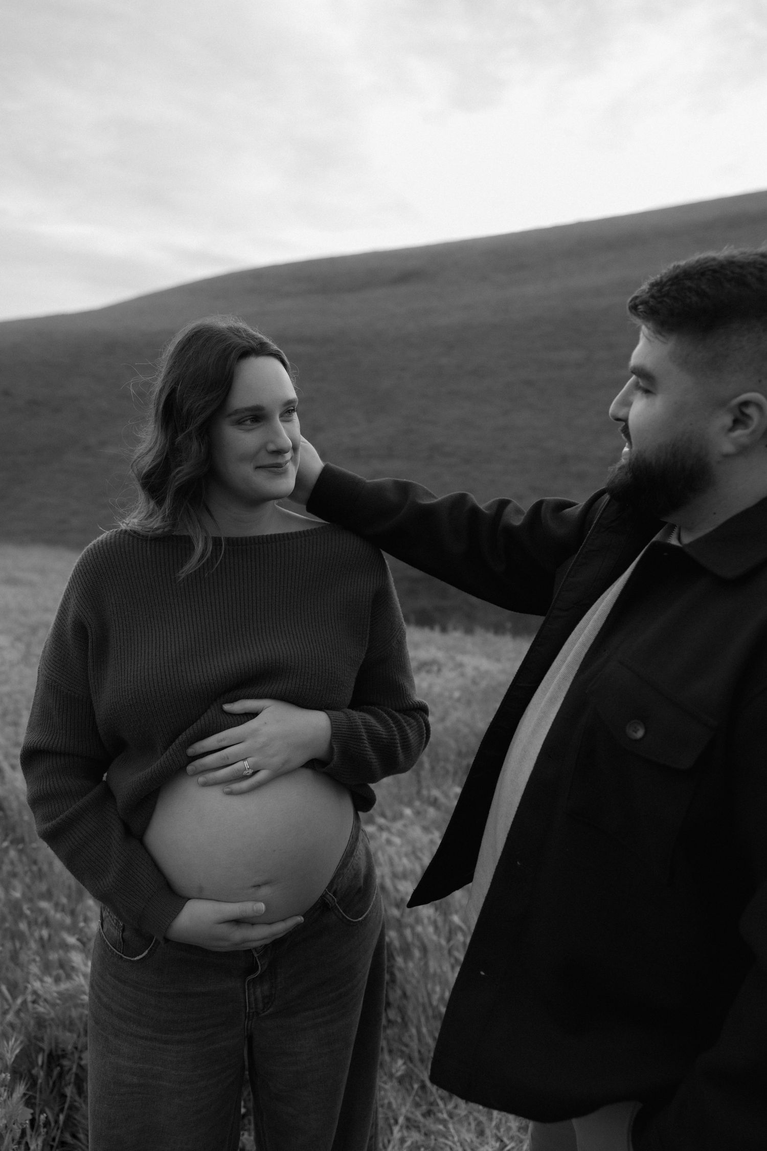 Black and white photo of a pregnant woman cradling her belly as her partner tenderly touches her face.