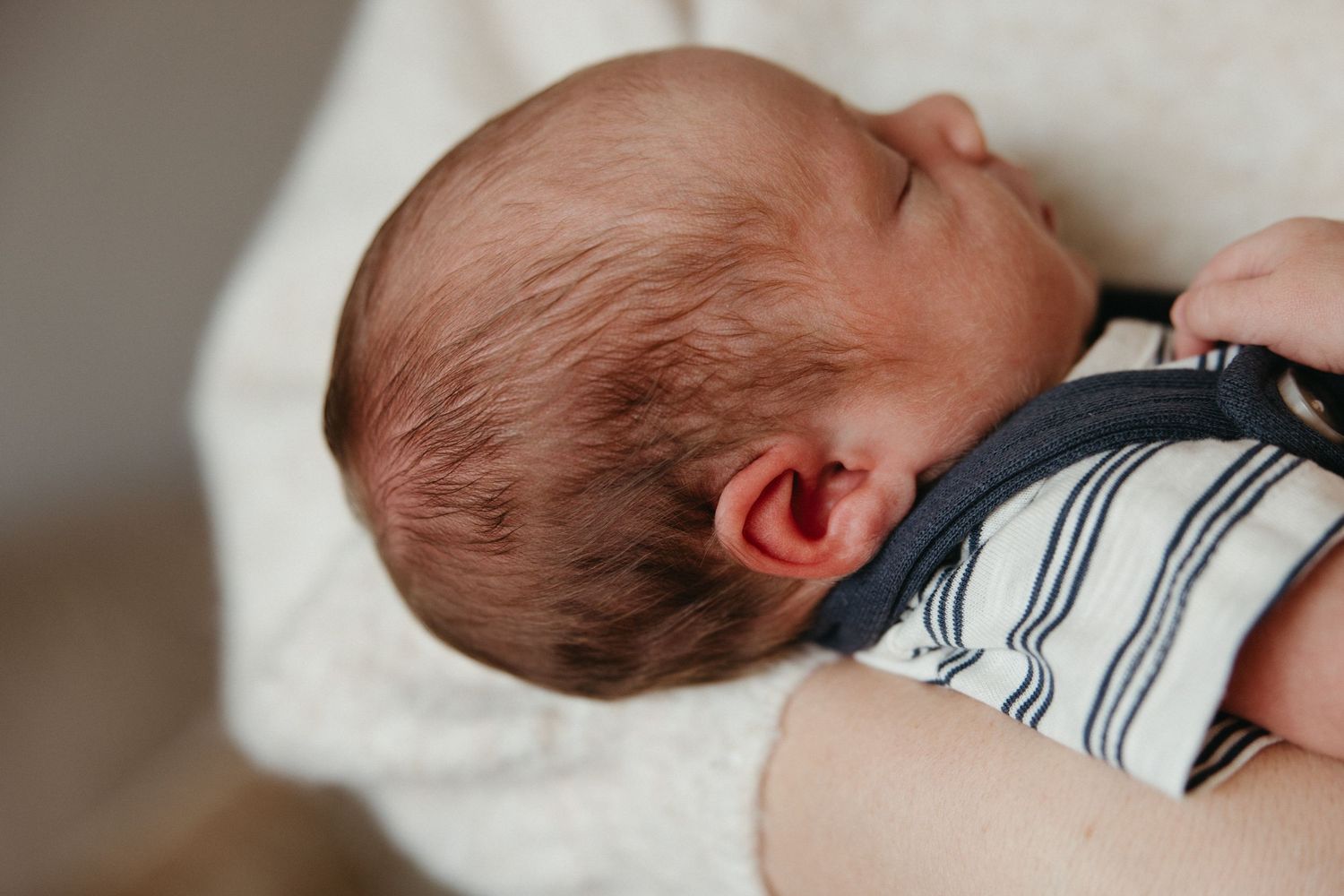 Close-up of a sleeping newborn baby with auburn hair wearing a striped outfit.