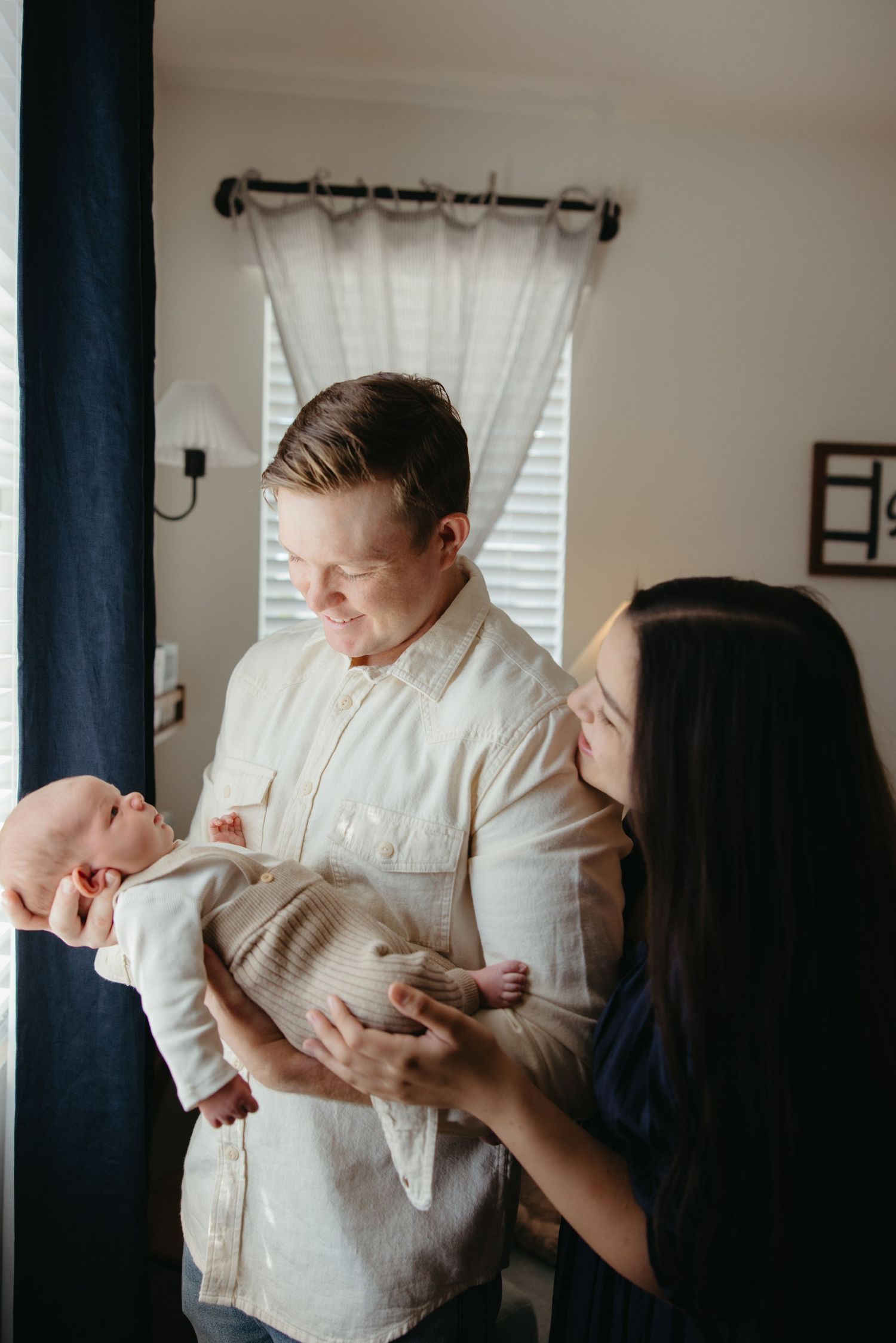 New parents smile lovingly at their newborn baby in a warmly lit home nursery.