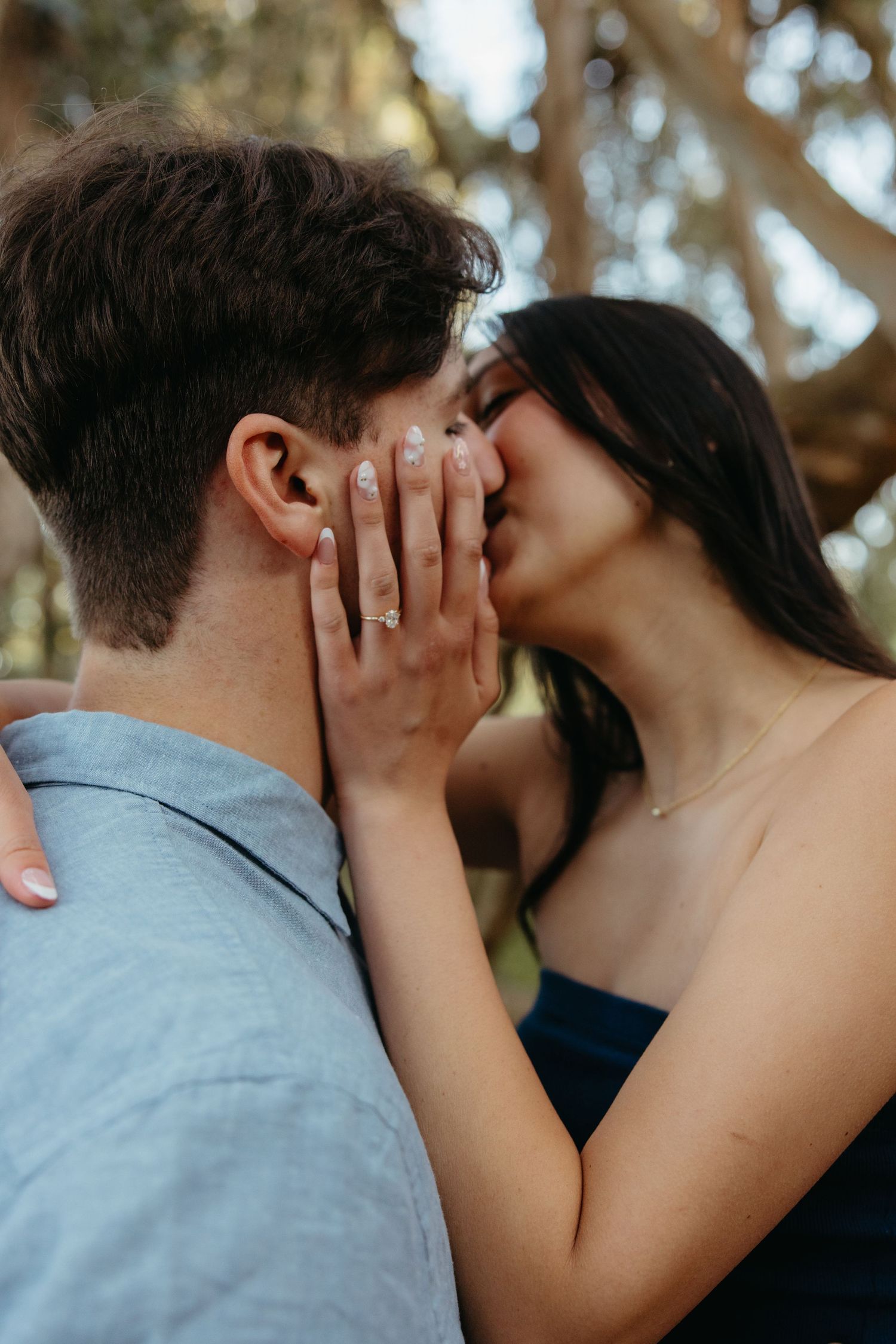 Close-up of couple sharing a kiss with womans engagement ring prominently displayed on mans cheek.