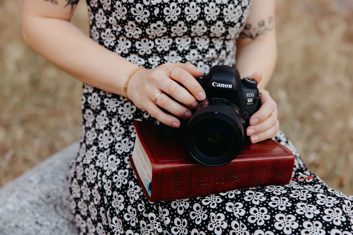 Close-up of woman in floral dress holding Canon DSLR camera resting on red book.