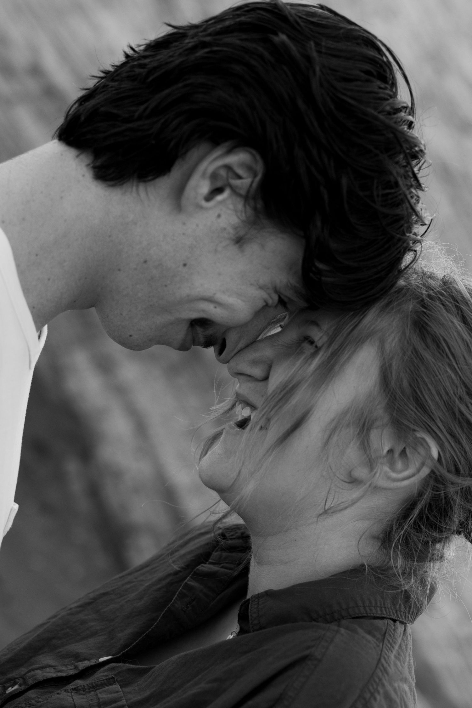 Black and white photo of a romantic couple leaning foreheads together, about to kiss outdoors.