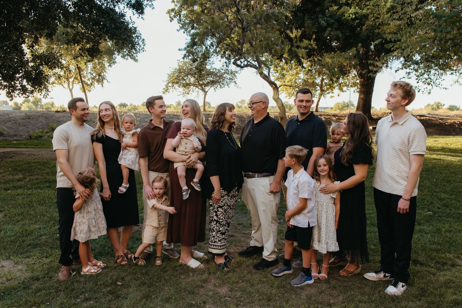 Large extended family group portrait outdoors under trees in warm golden light.