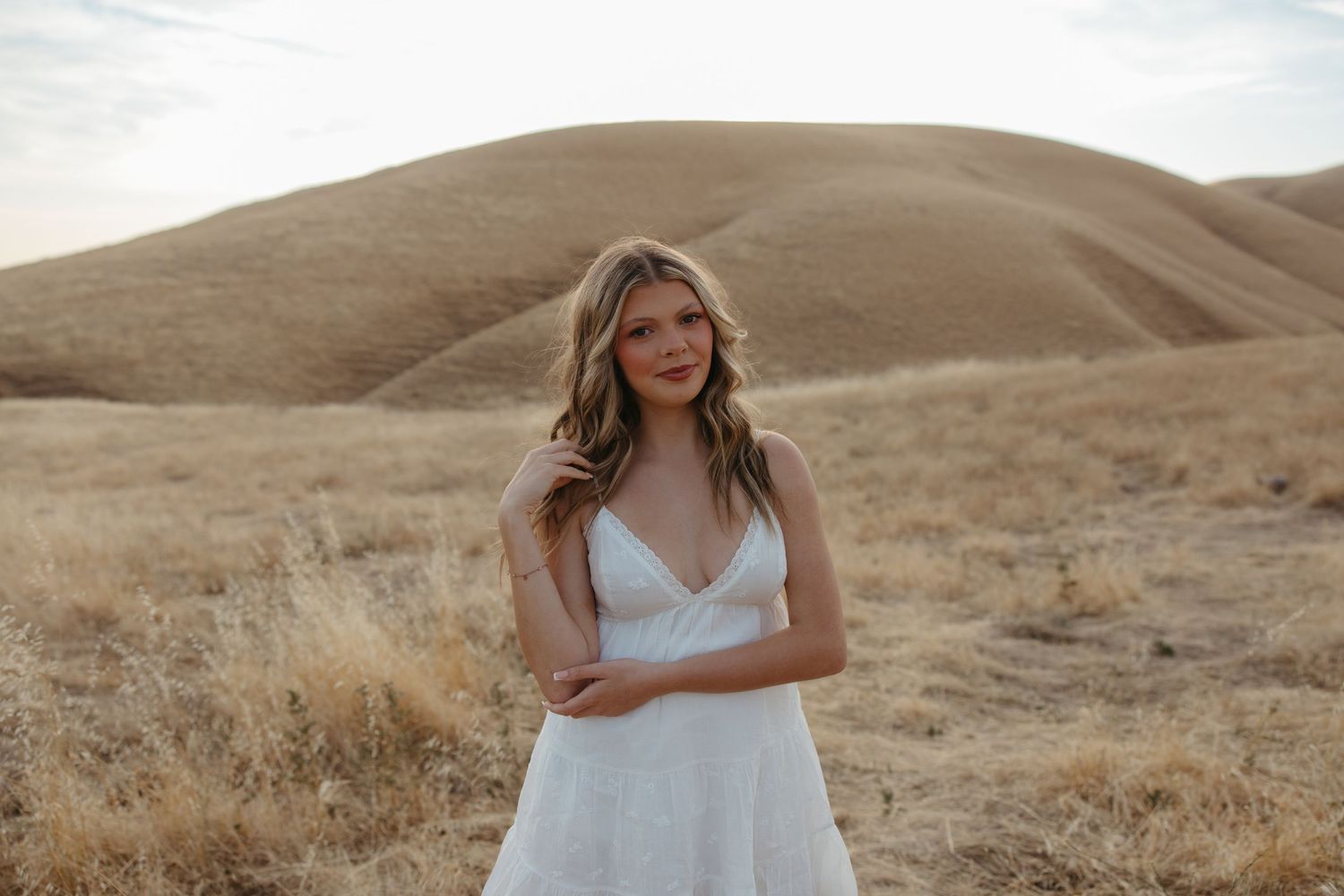 Bride in a white lace gown posing in a golden field with rolling hills in the background.