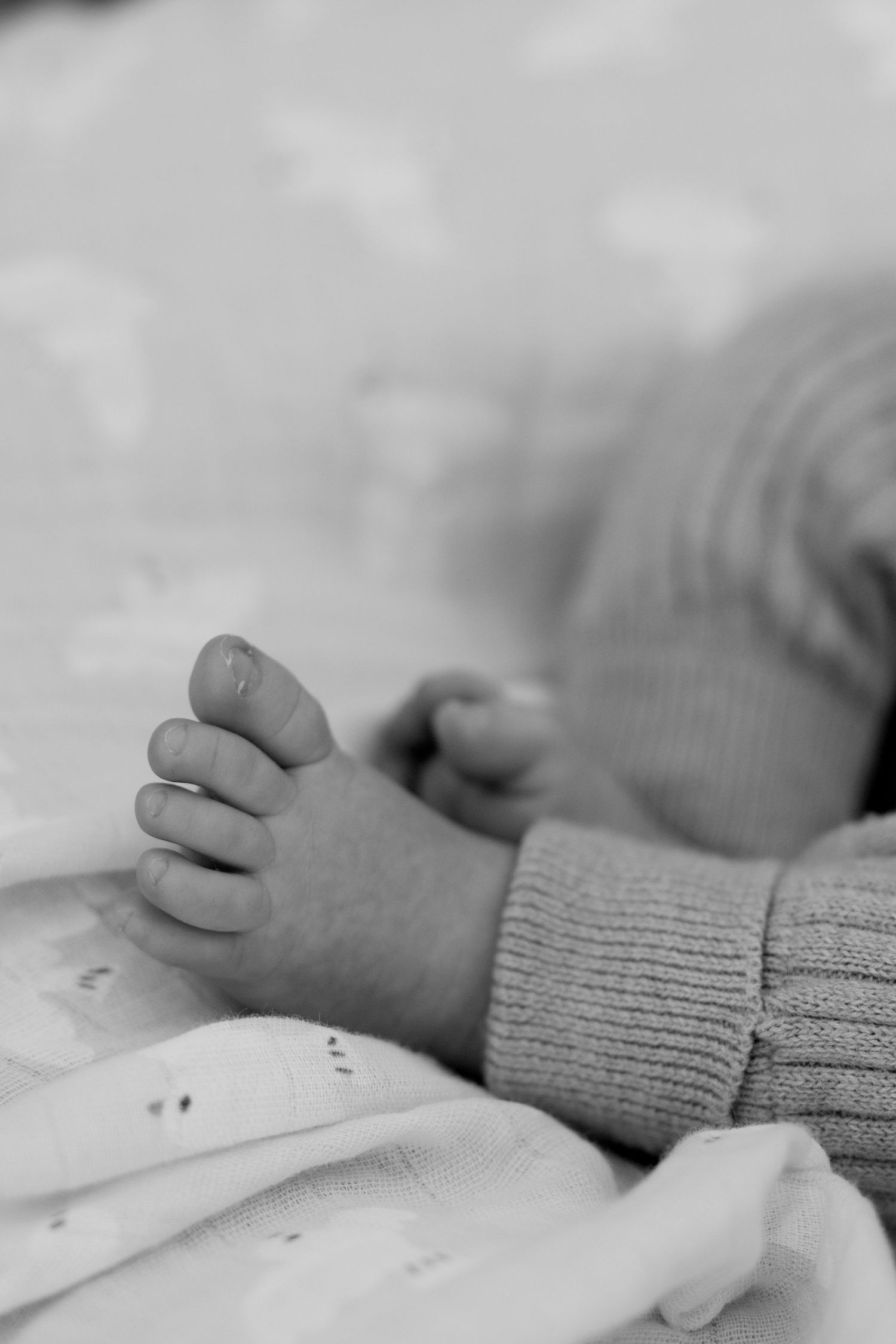 Close-up black and white photo of a newborn babys tiny feet and toes in a knit outfit.
