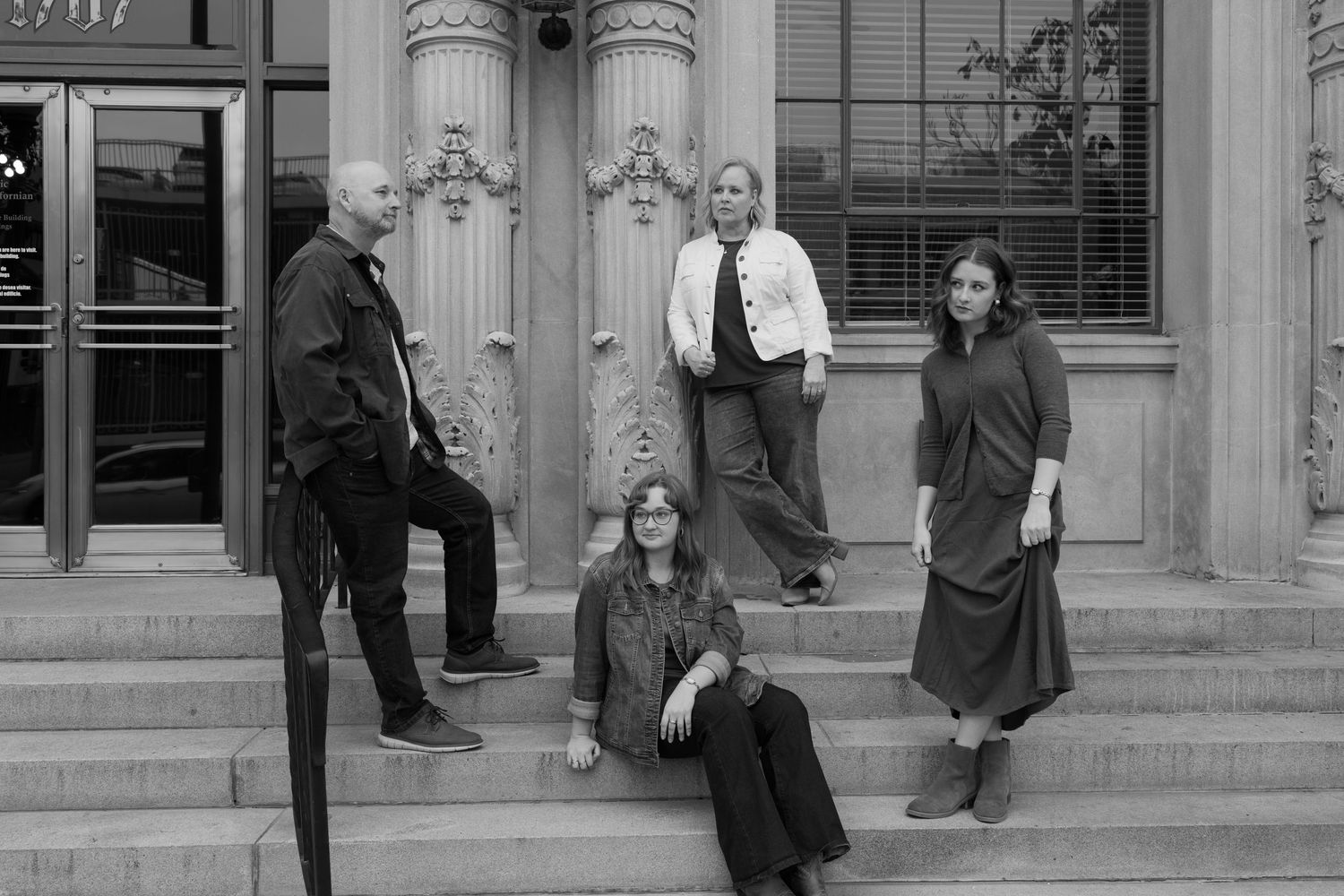 Black and white photo of four people posing on steps of a classic stone building exterior.