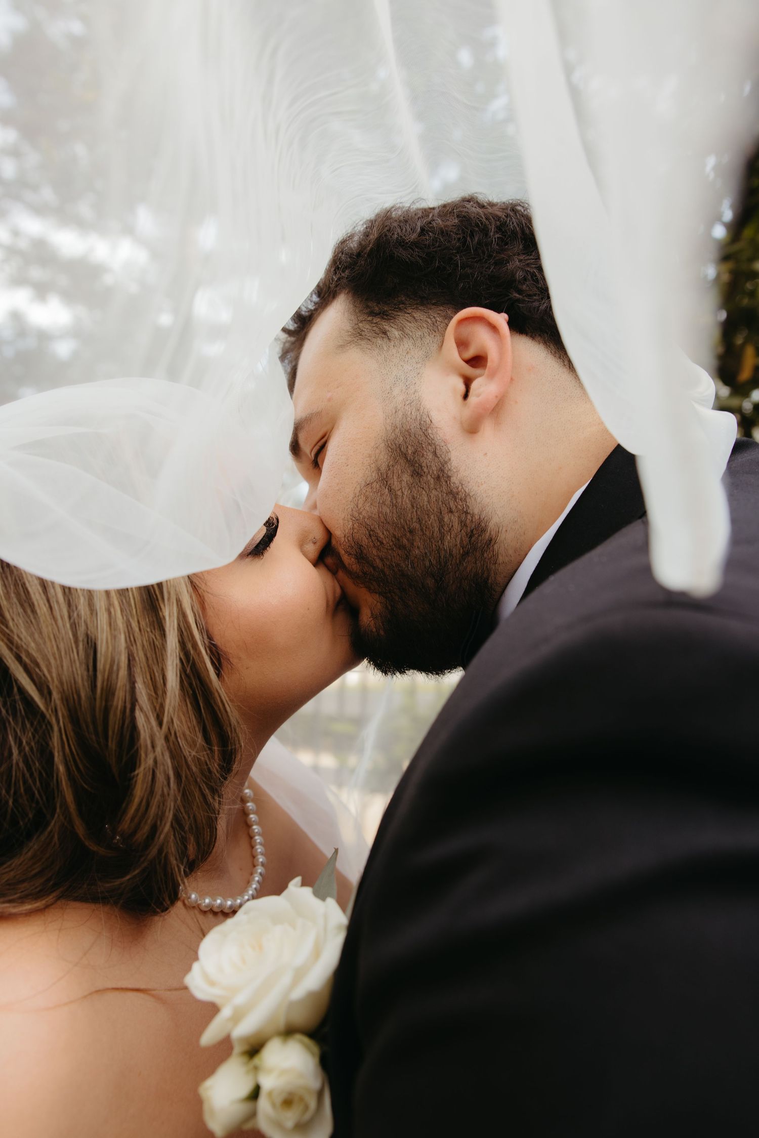 Bride and groom sharing a romantic first kiss under a flowing white veil at their wedding.