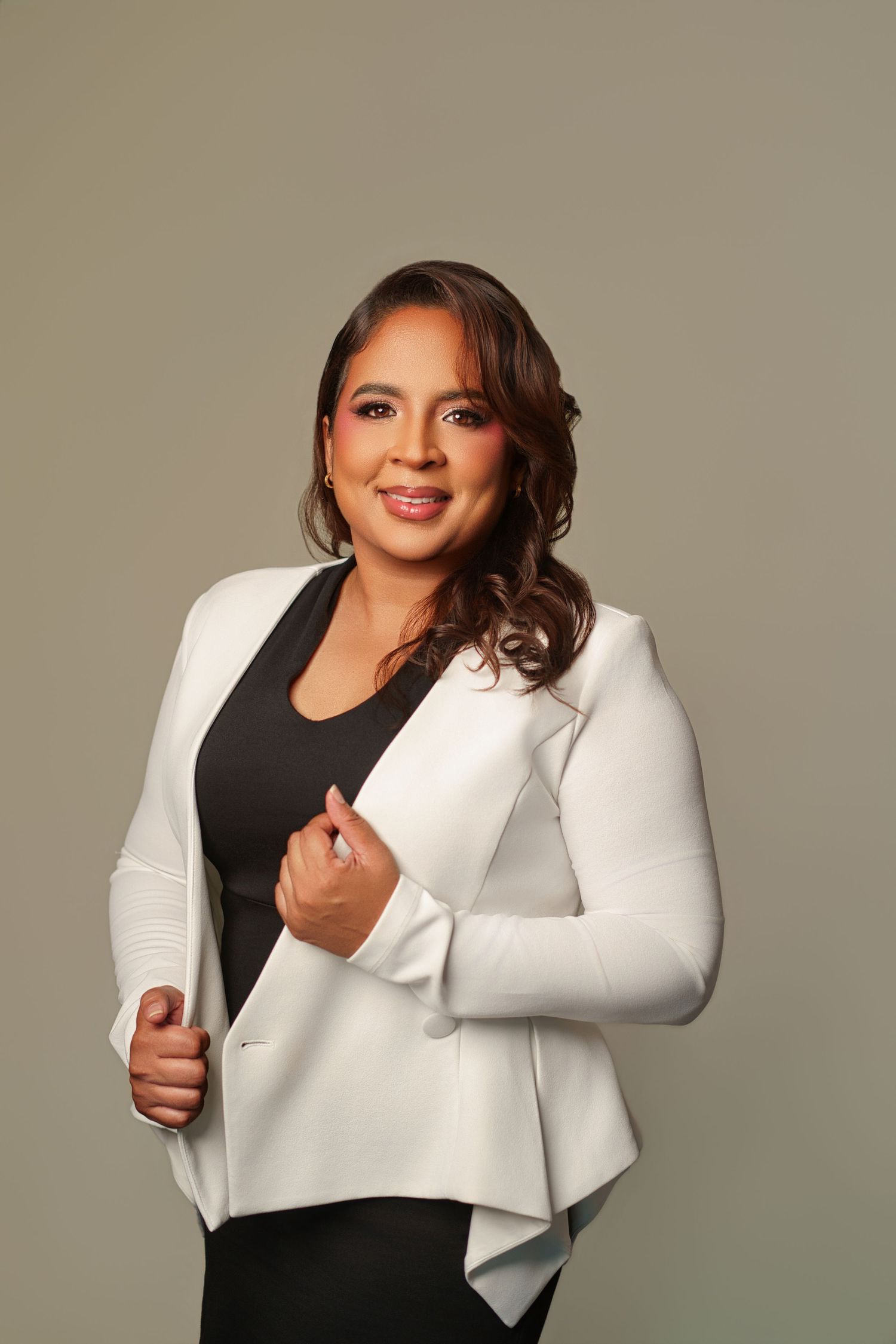 Professional woman in white blazer and black top smiling confidently in a studio portrait setting.