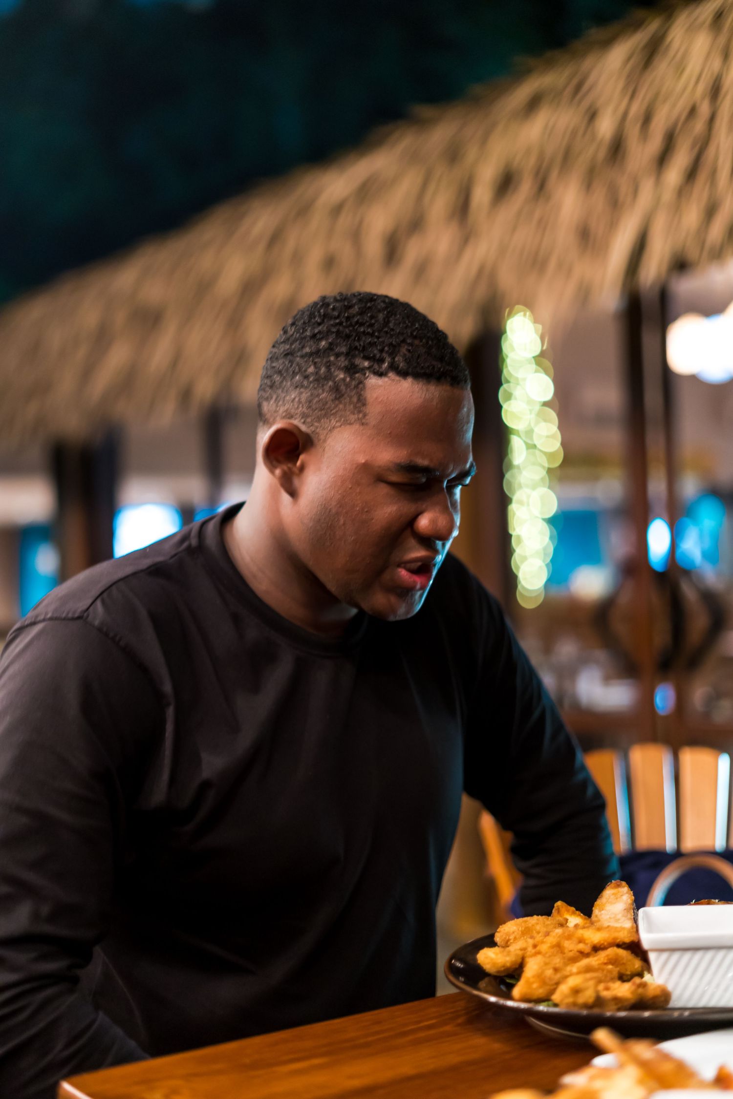 A person in a black shirt sits at a restaurant table examining food in dim ambient lighting.