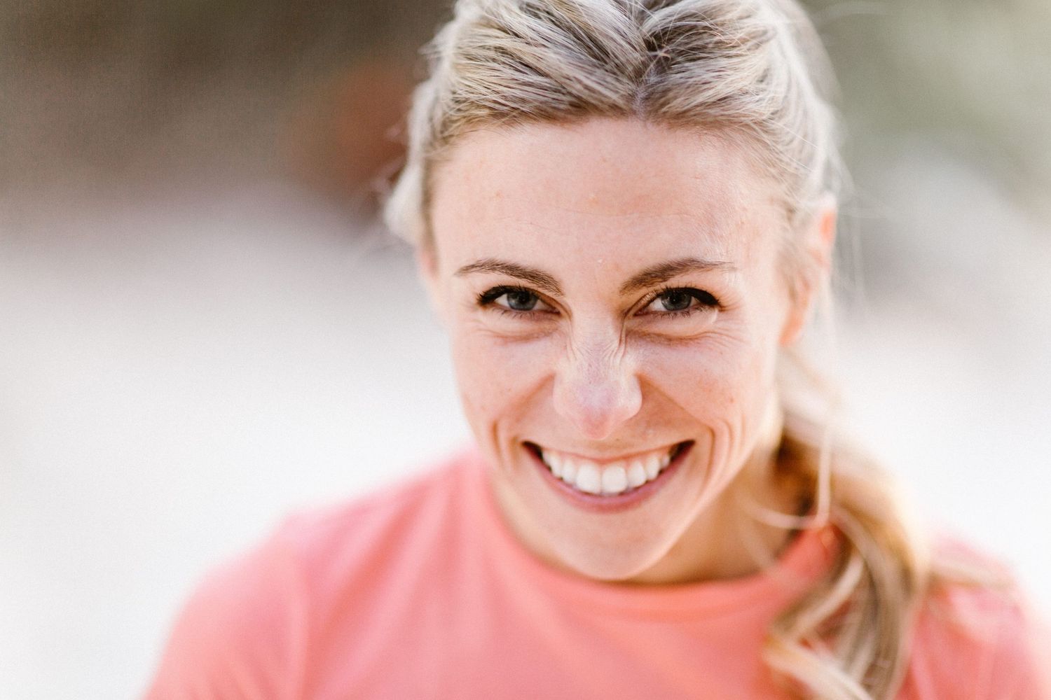 Smiling blonde woman in pink shirt with freckles outdoors in natural light.