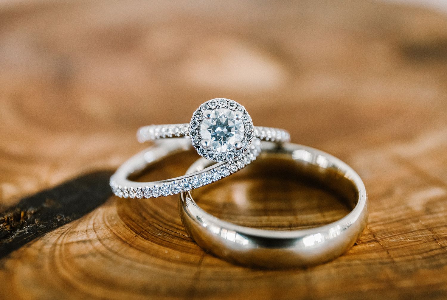 Elegant diamond halo engagement ring and wedding band set displayed on a rustic wooden surface.