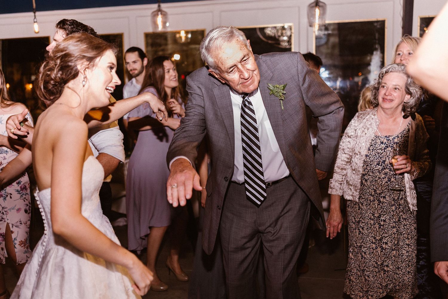 Bride dances joyfully with older man in suit at lively wedding reception celebration.
