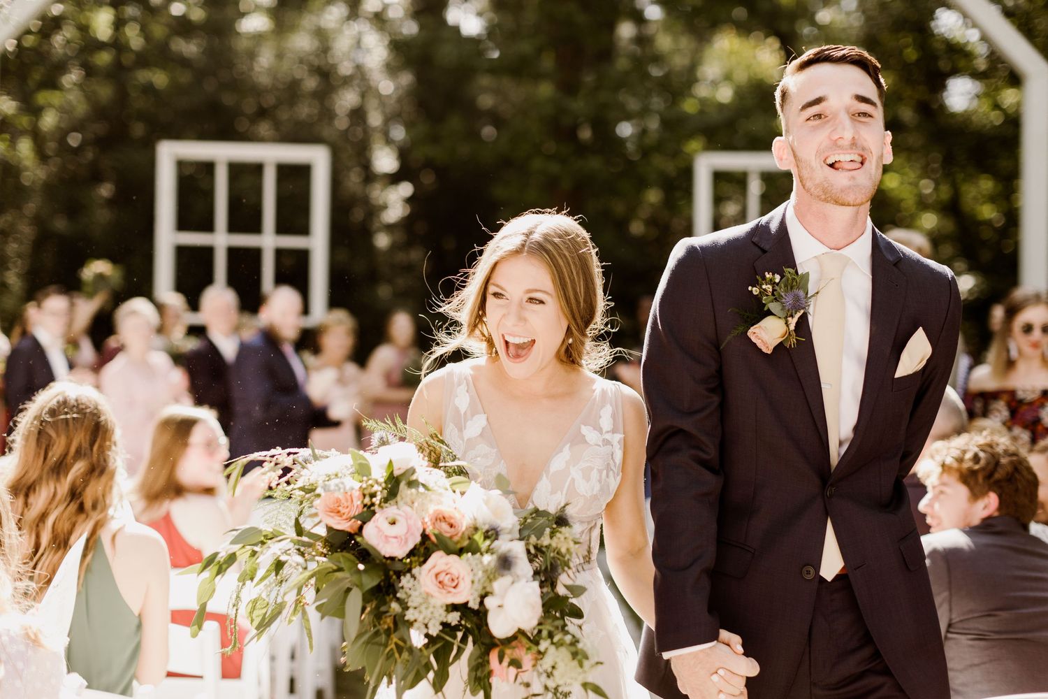 Joyful bride and groom walk back down the aisle after wedding ceremony in outdoor garden setting.