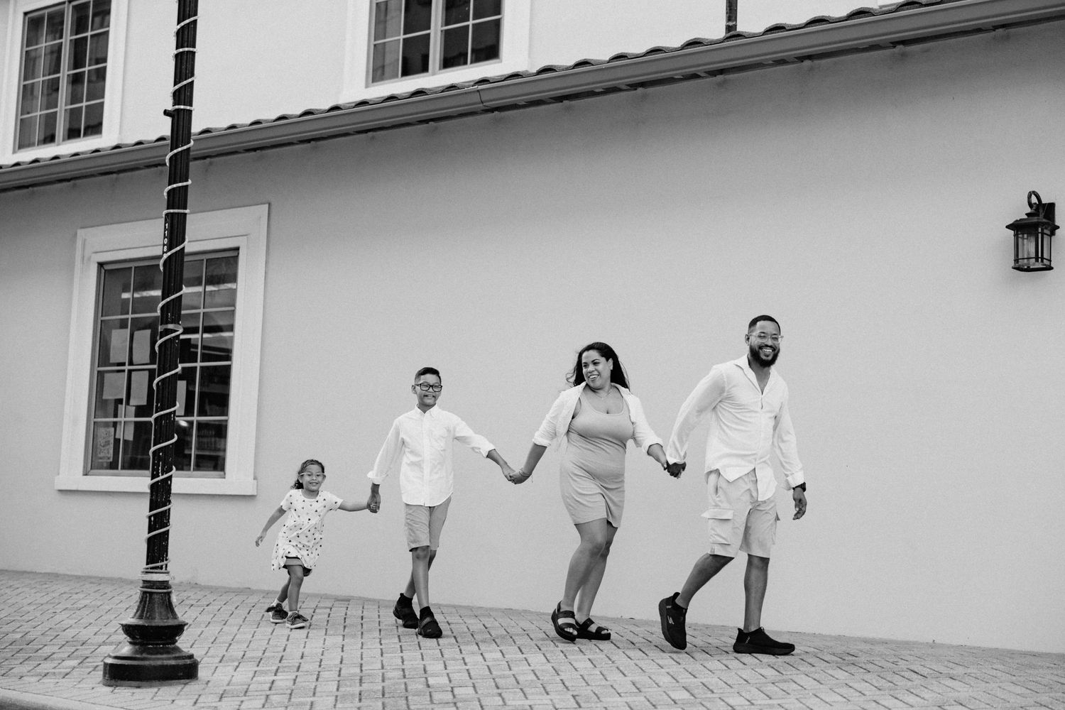 Black and white photo of a family of four holding hands and walking past a building.