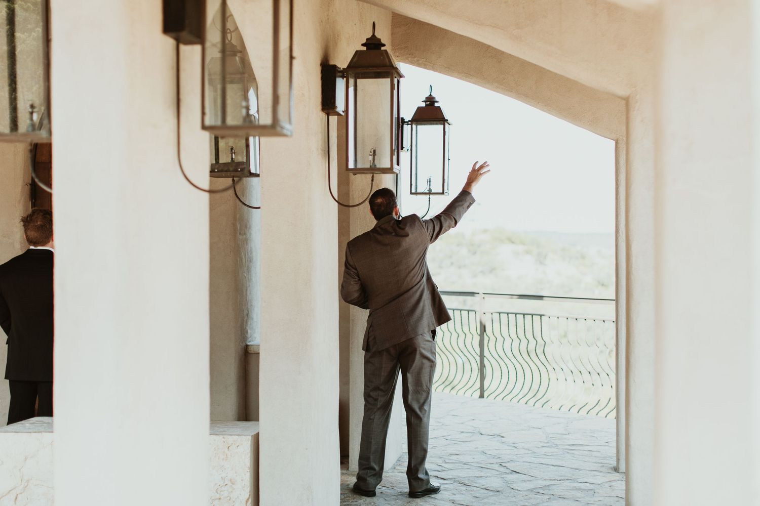 Man in suit gesturing toward elegant outdoor lanterns at a upscale venue entrance.