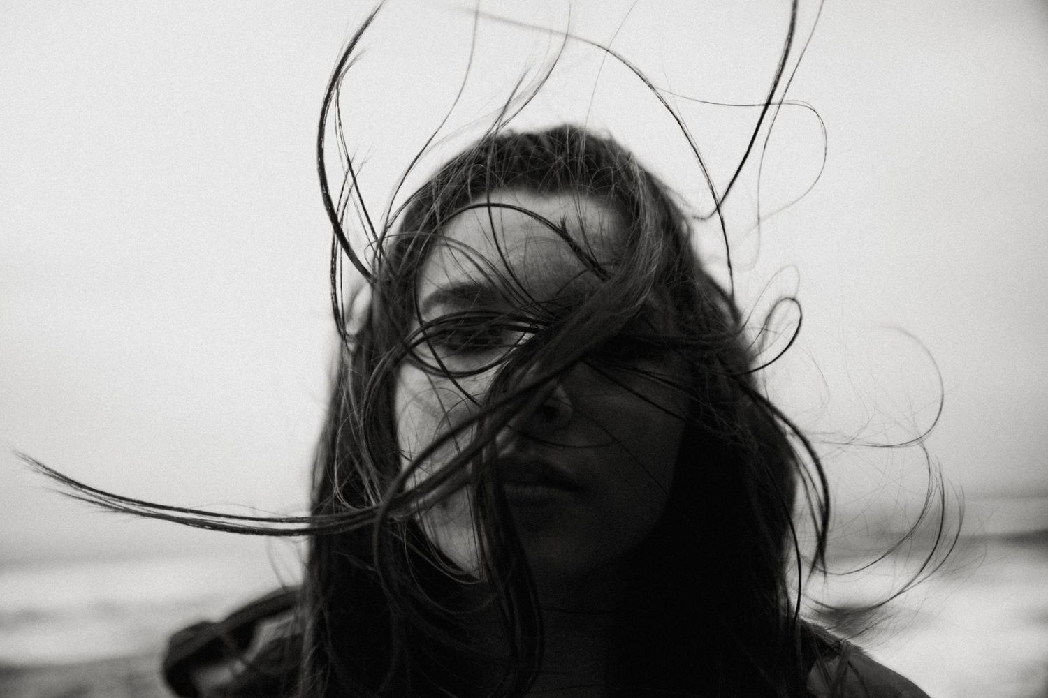 Black and white portrait of a woman with long dark hair blowing across her face in the wind.