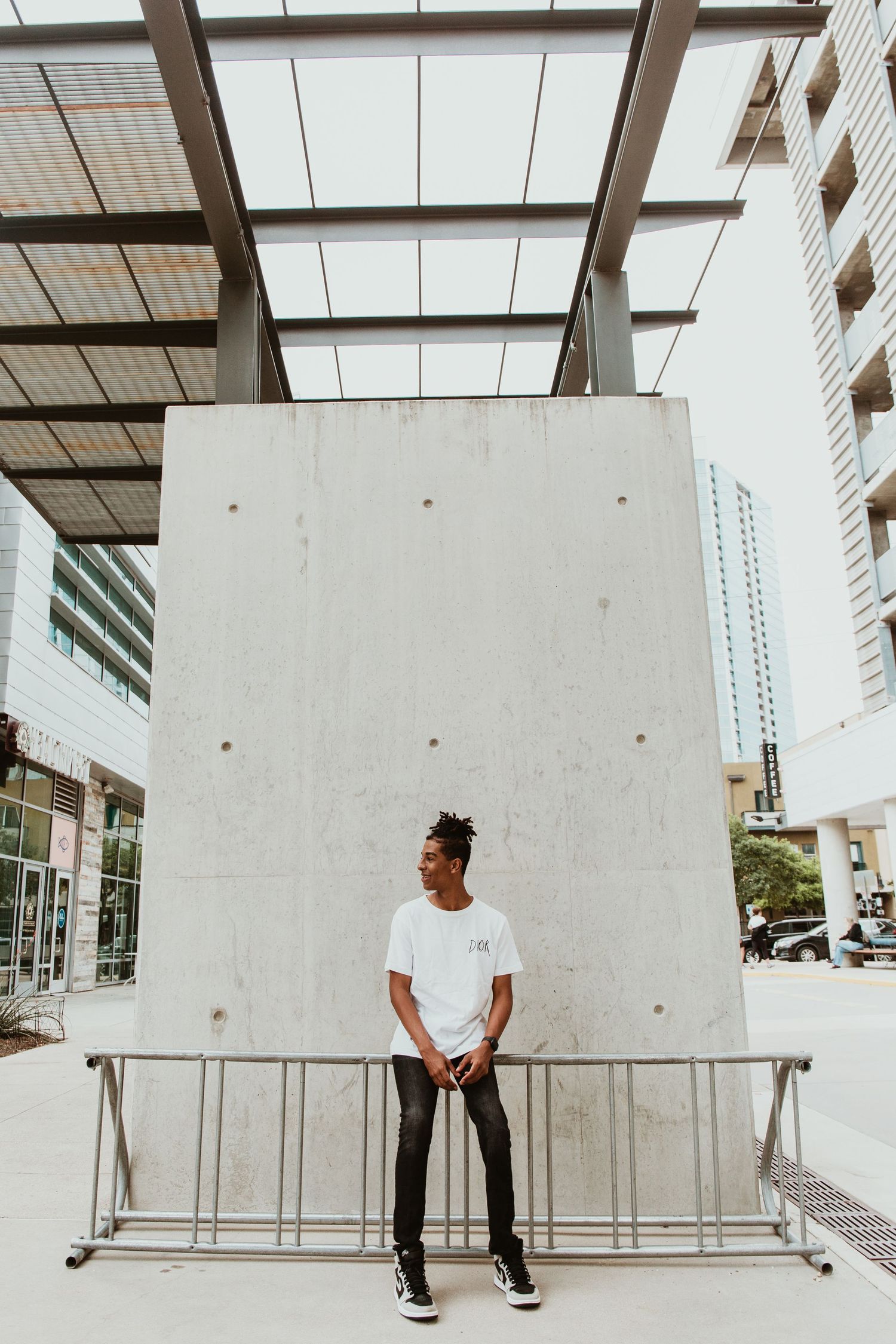 Young man in white t-shirt standing against large concrete wall in modern urban plaza.