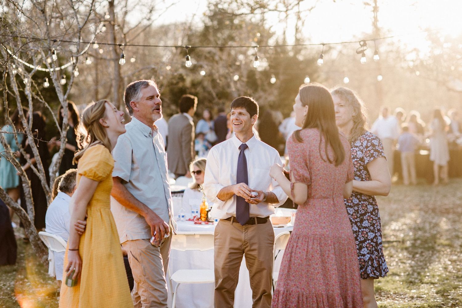Family members gather and converse in golden hour light at an outdoor wedding celebration.