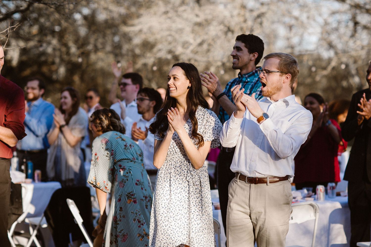 Wedding guests in outdoor setting applauding and celebrating during daytime wedding reception ceremony.