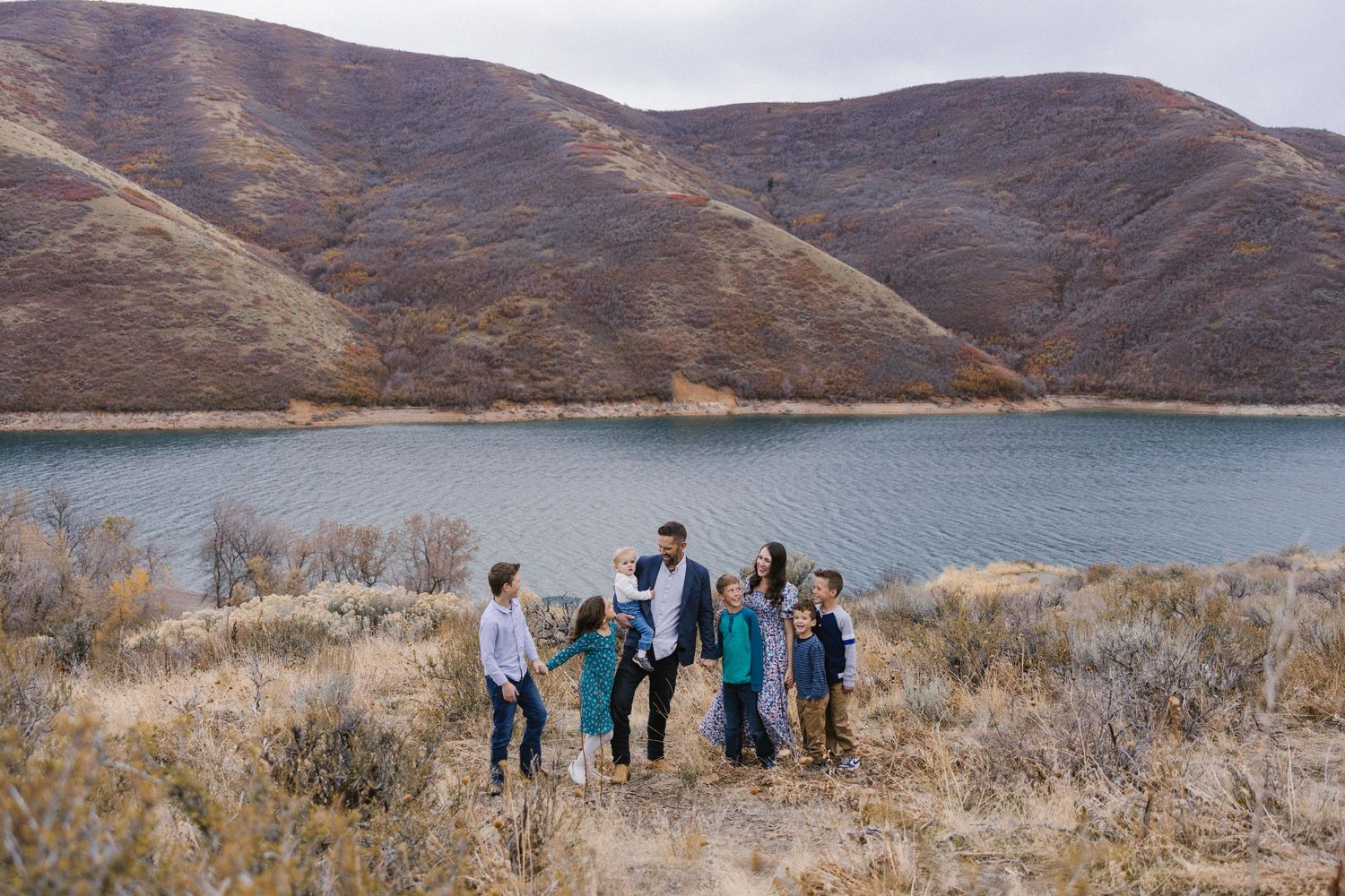 Large family group standing together near a lake with brown hills in the background.