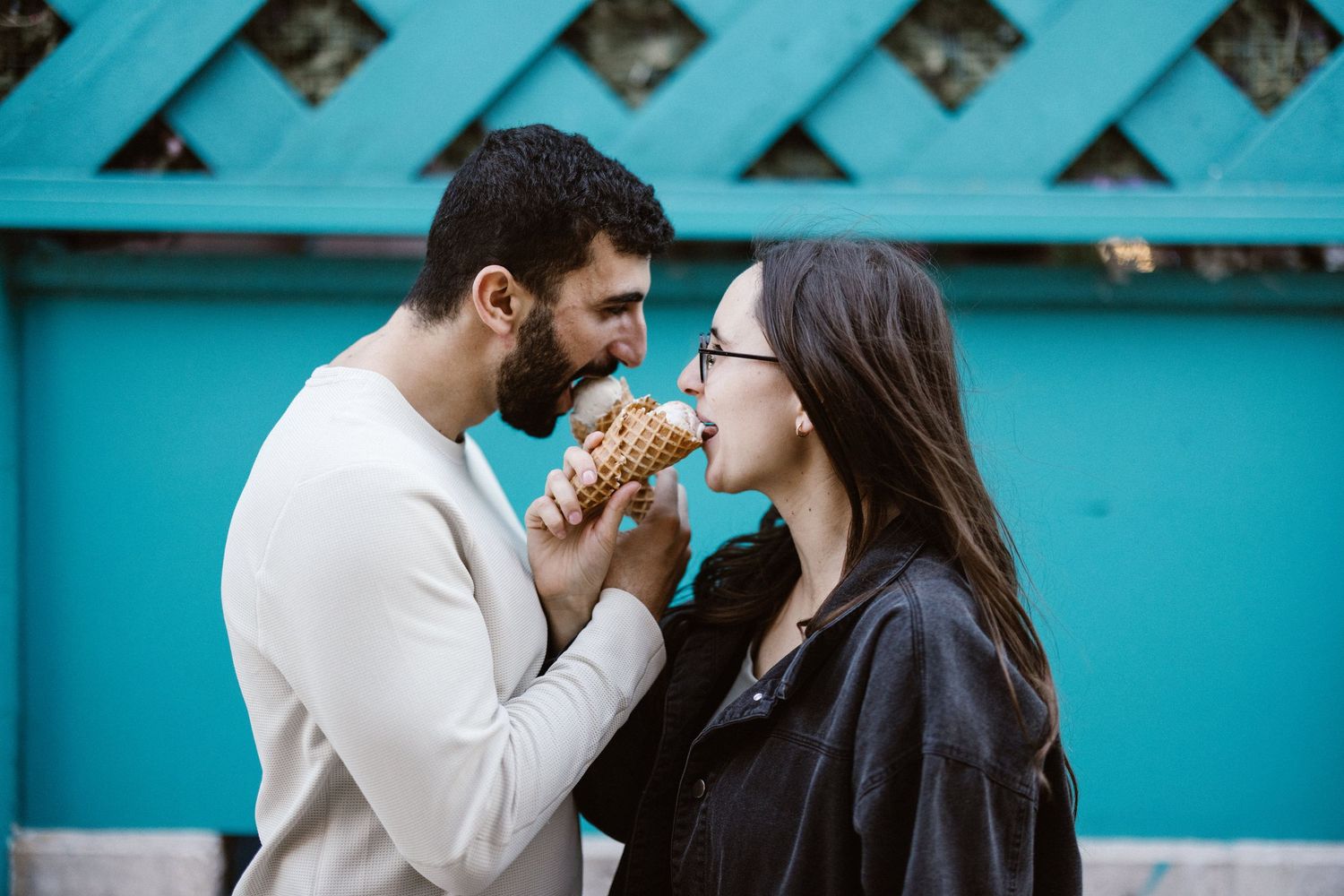 Couple sharing an ice cream cone together against a turquoise wall.
