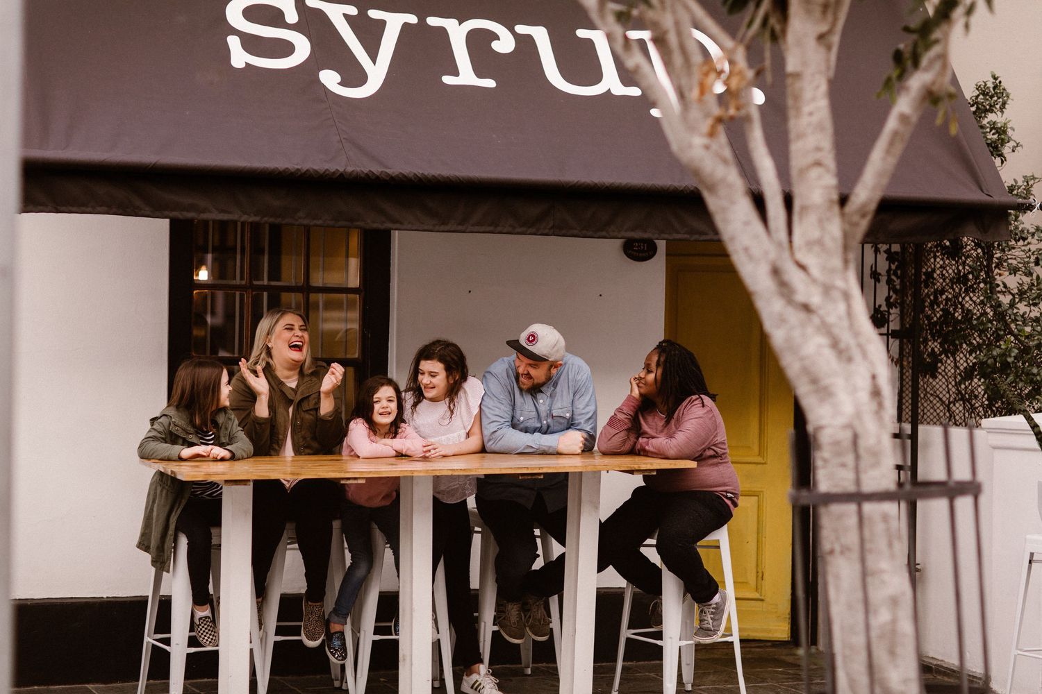 Family of five laughing and leaning on a high table outside a cafe called Syrup.
