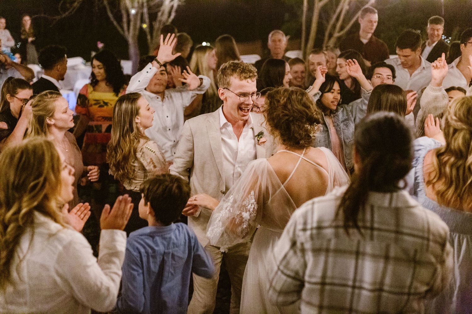 Bride and groom celebrating joyfully with guests on outdoor wedding dance floor.