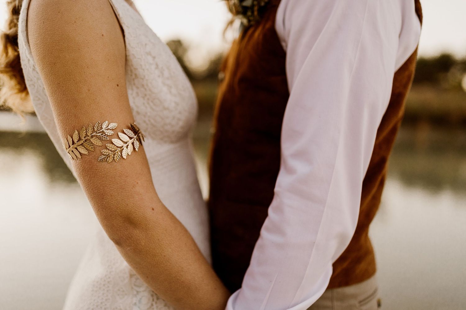 Bride and groom holding hands, bride wearing gold leaf arm cuff bracelet in boho wedding style.