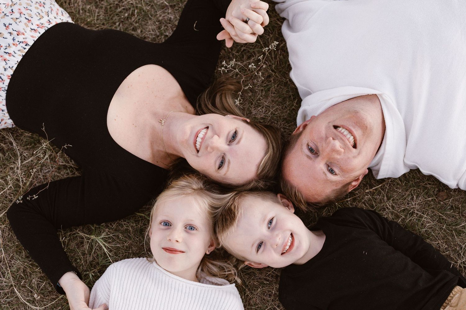 Aerial view of a smiling family of four lying together on grass, parents and two young children.