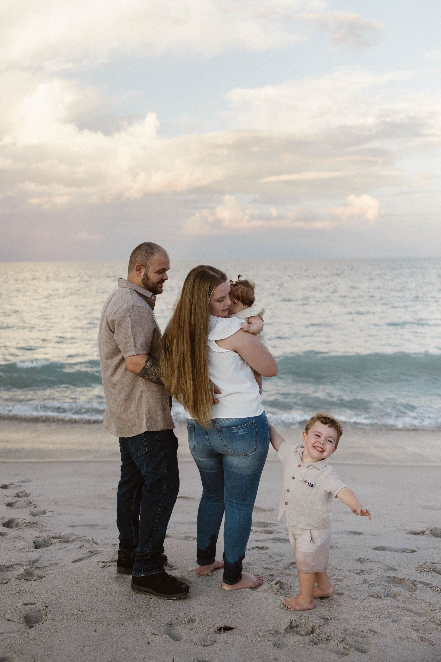A family of four enjoys a peaceful moment on a sandy beach at sunset with gentle ocean waves.