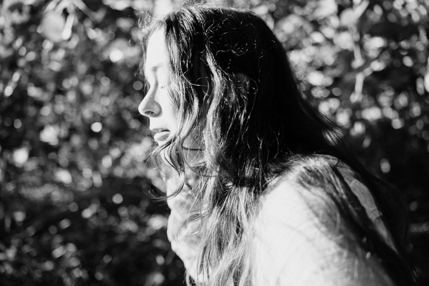 Black and white close-up profile of a young woman with long flowing hair against a leafy background.