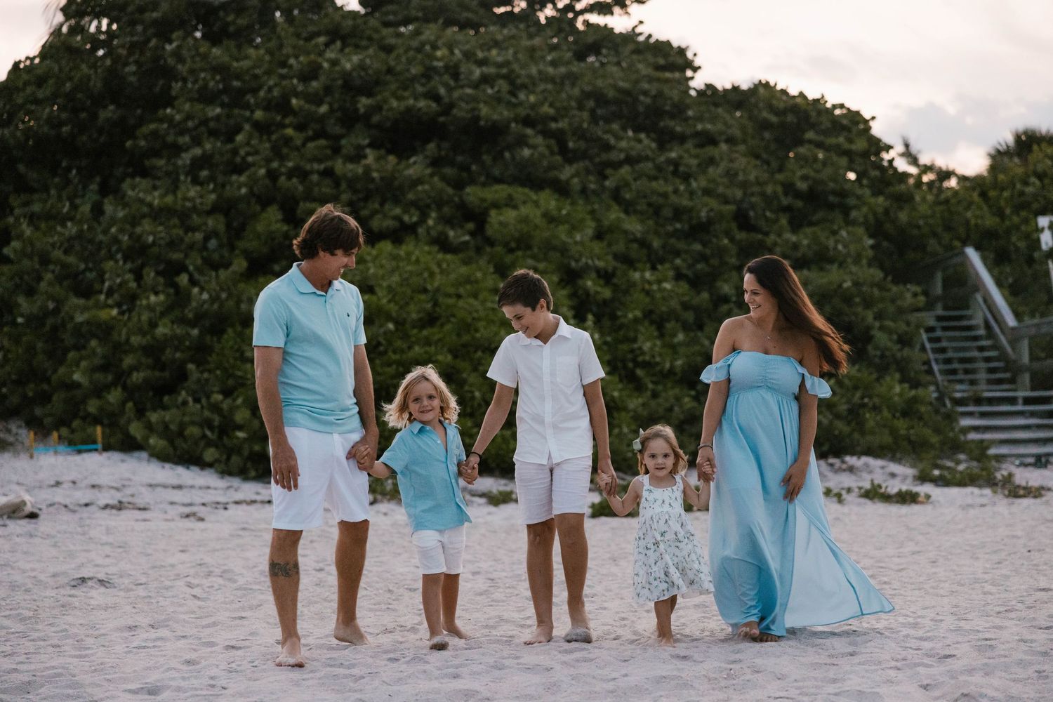 A family of five in matching aqua outfits walking on a white sandy beach.