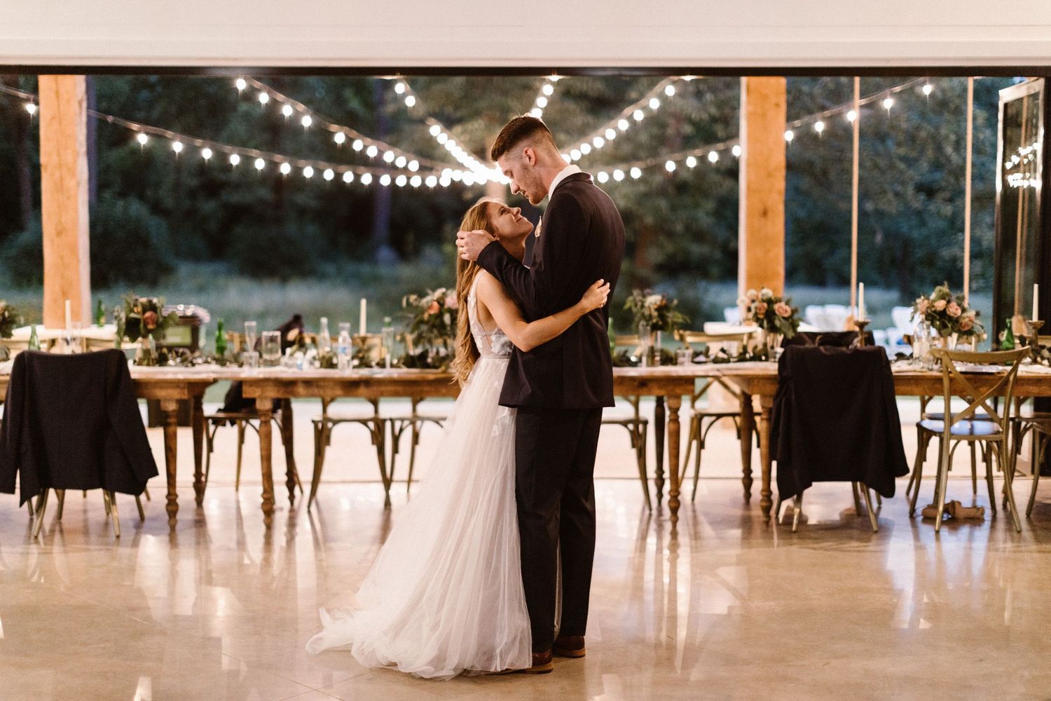 Bride and groom sharing first dance under string lights in elegant reception venue.