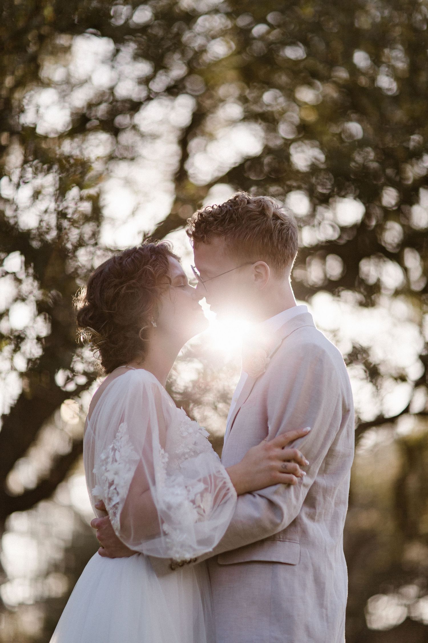 Bride and groom sharing a romantic moment about to kiss with golden sunlight glowing behind them.