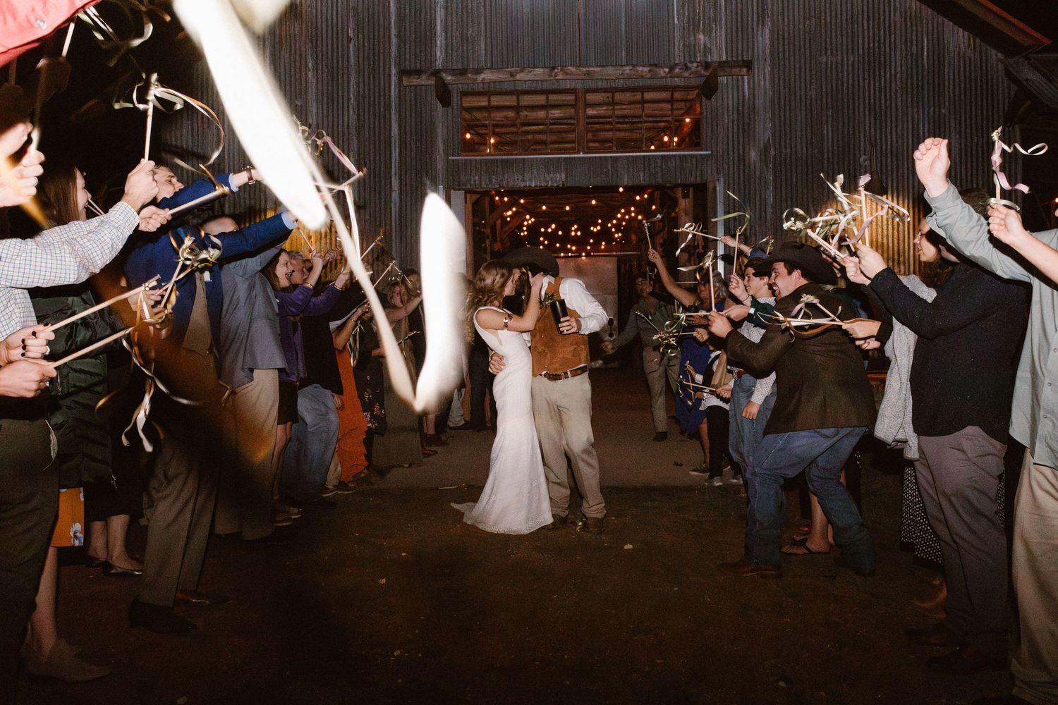 Bride and groom exit through sparkler tunnel in rustic barn wedding send-off at night.