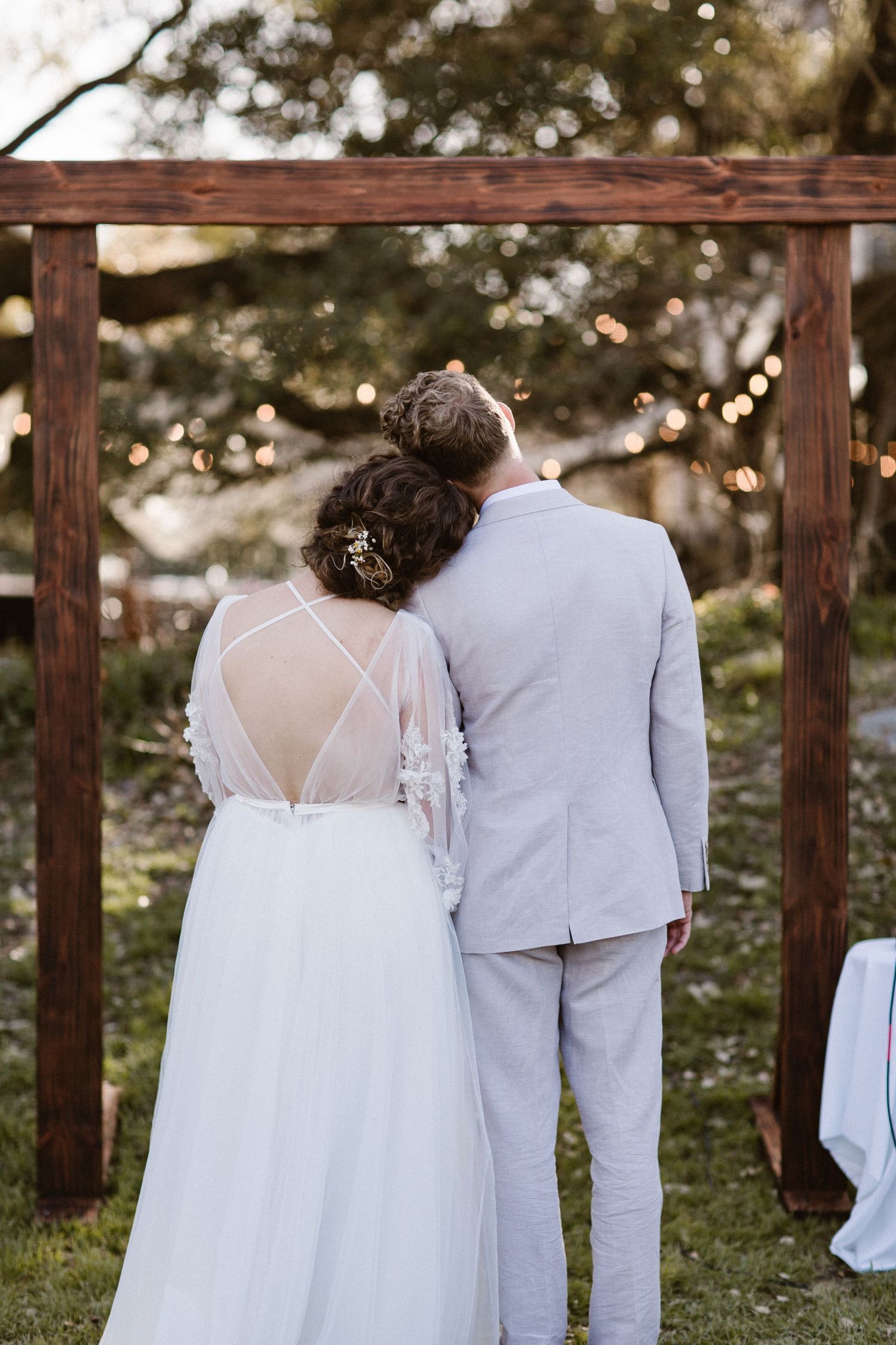 Bride and groom stand together under a rustic wooden arch at their outdoor wedding ceremony.